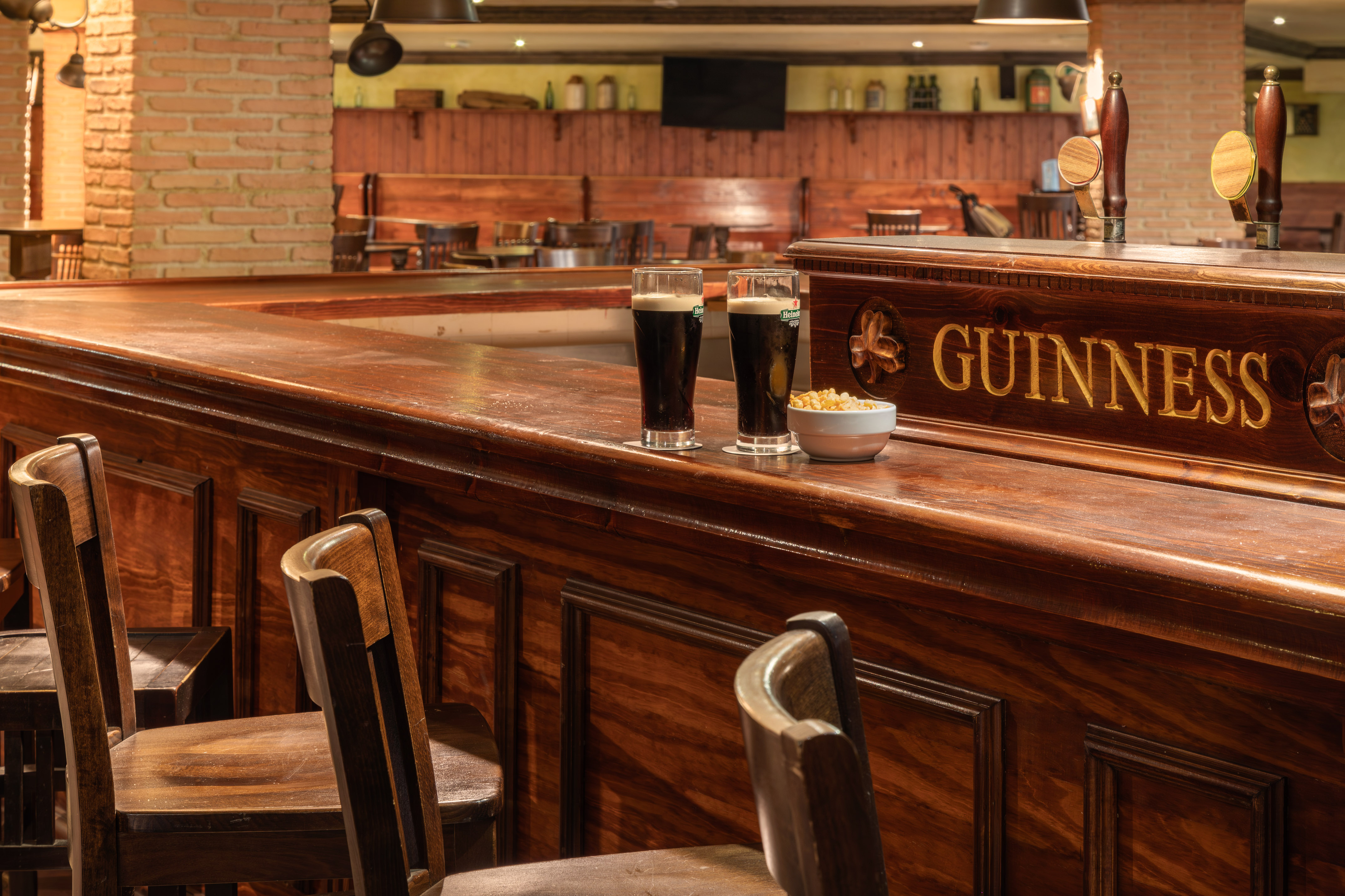 Two Guinness stout beers and snacks on a polished wooden pub bar.