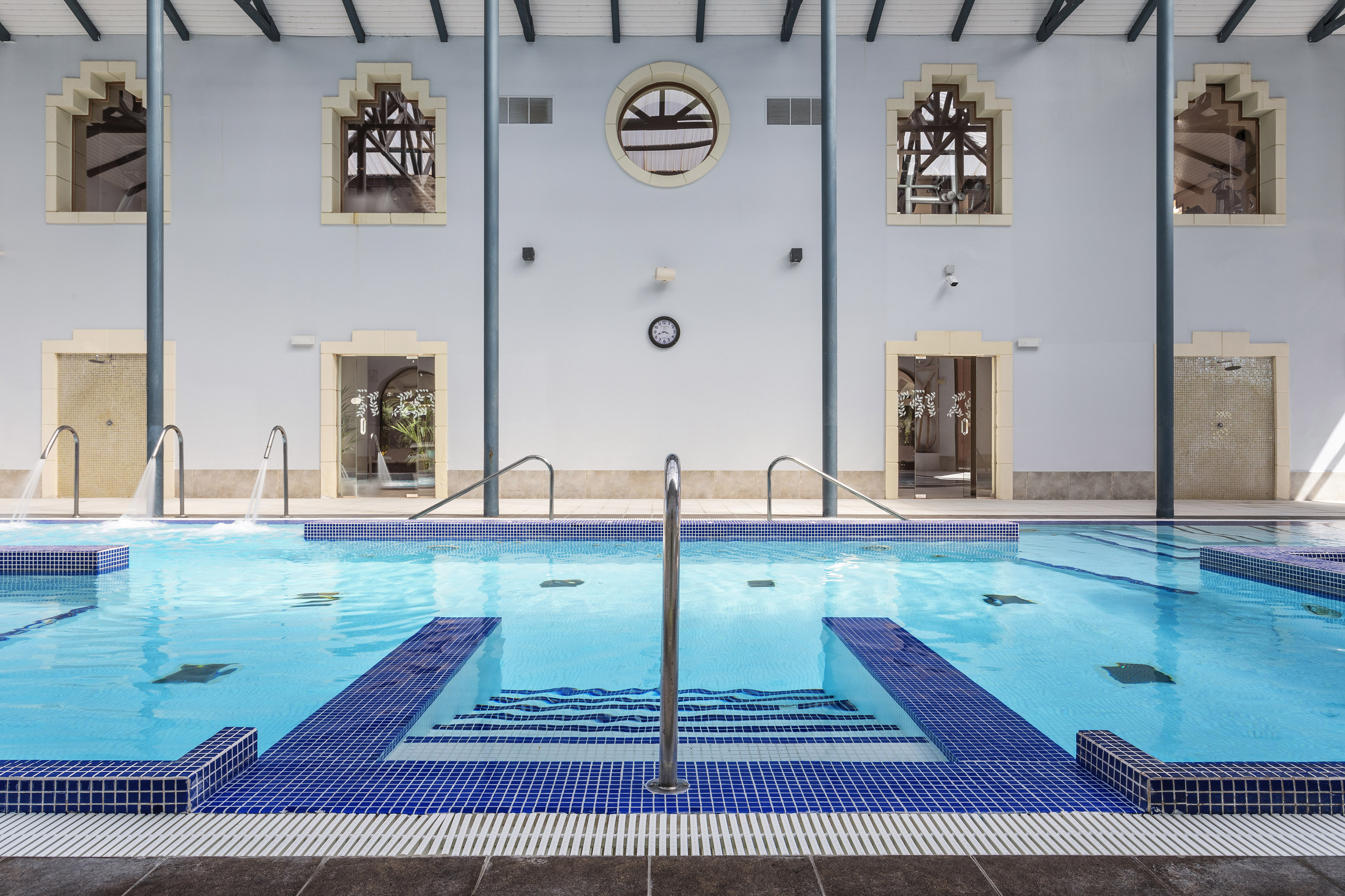 Indoor spa pool with blue mosaic tiles, water jets, and architectural windows.