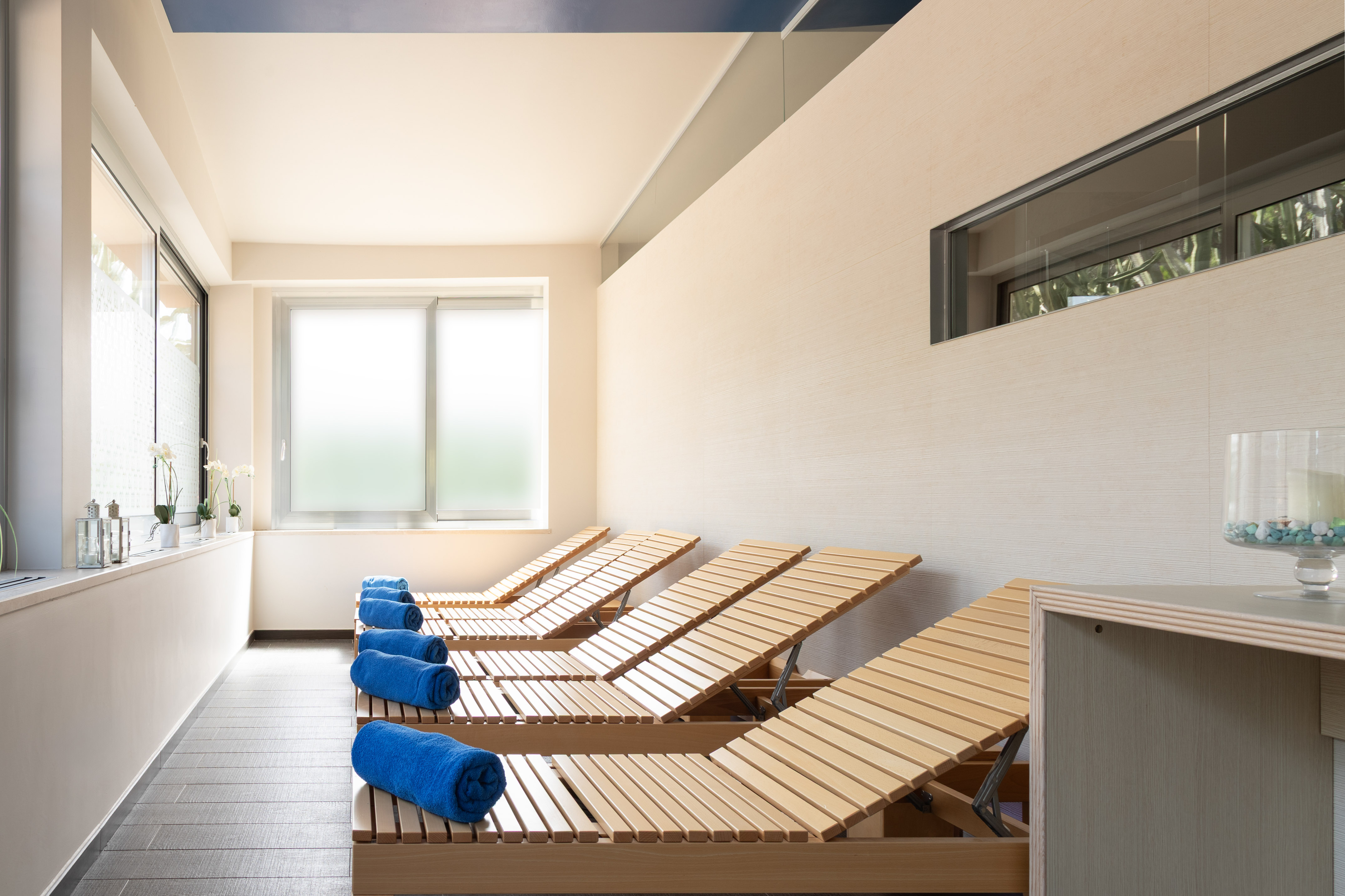Spa relaxation room with wooden lounge chairs, blue towels, and natural light.