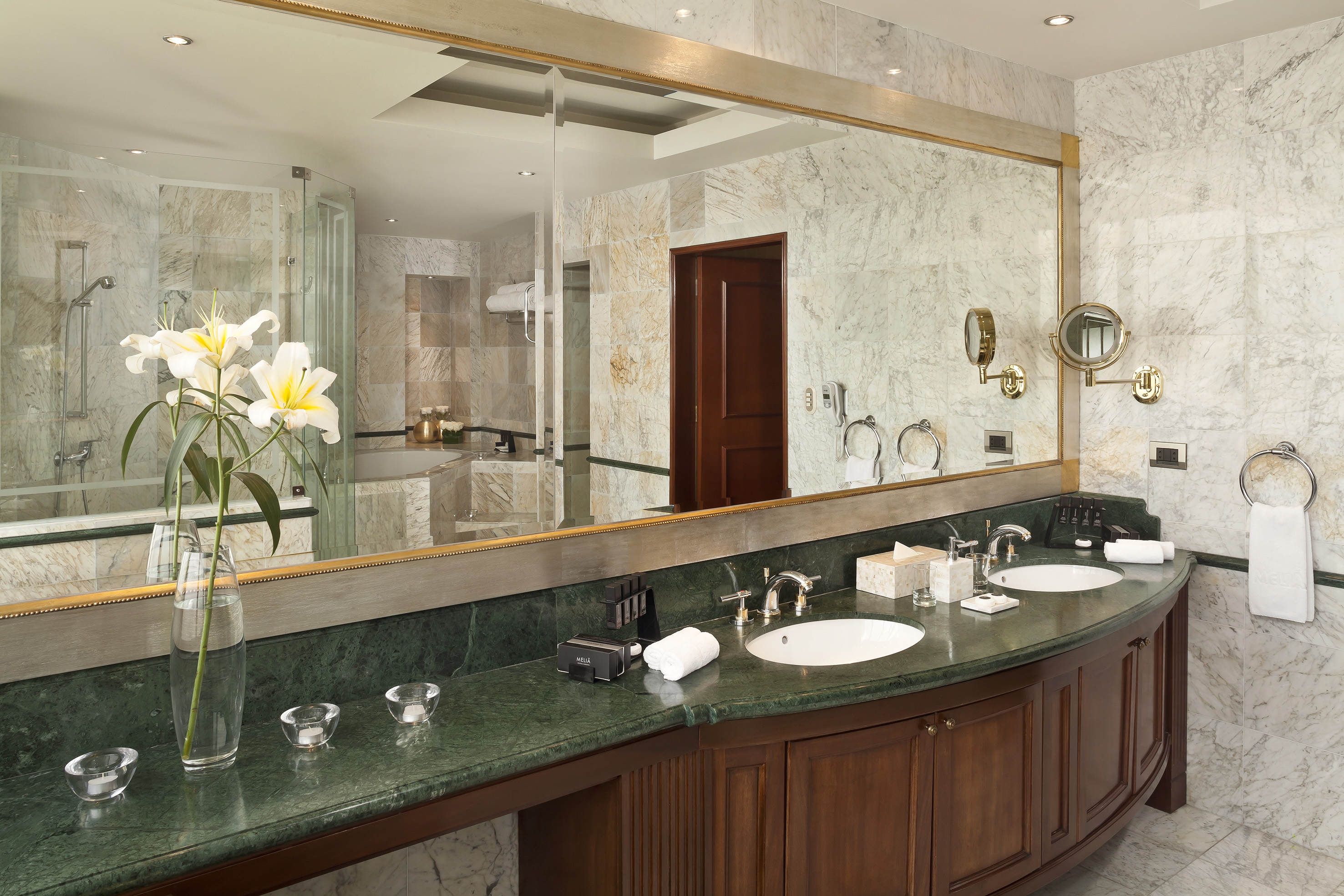 Luxury hotel bathroom with double green marble vanity, large mirror, and white lilies.