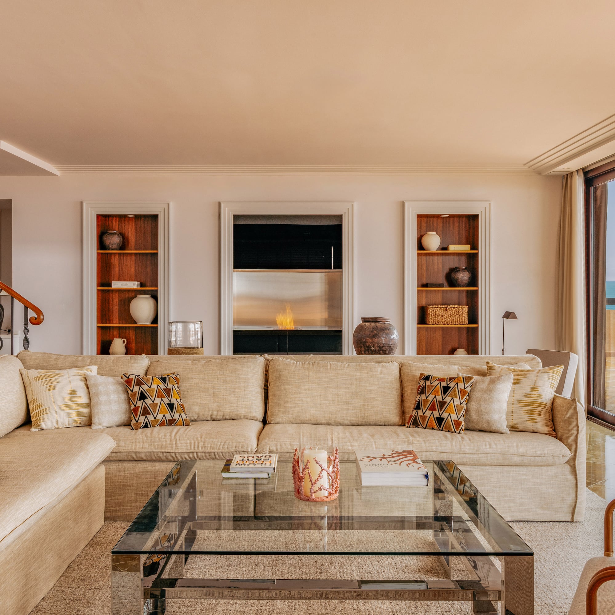 Spacious living room with beige sofa, modern fireplace, and ocean view balcony.