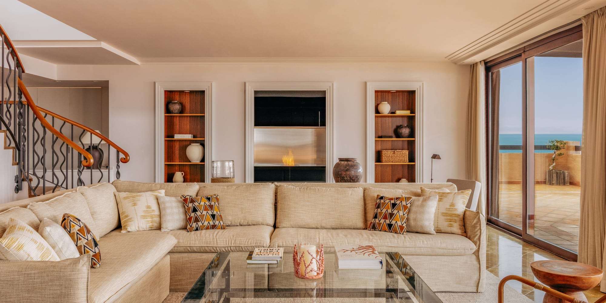 Spacious living room with beige sofa, modern fireplace, and ocean view balcony.