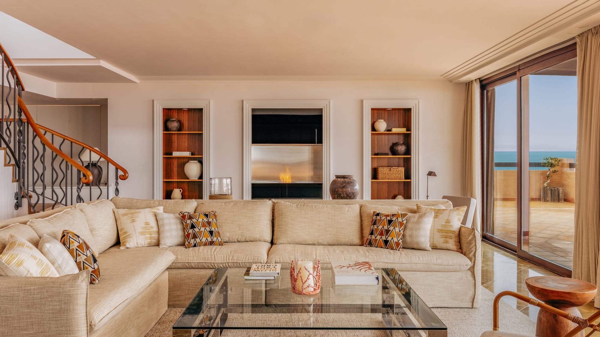 Spacious living room with beige sofa, modern fireplace, and ocean view balcony.