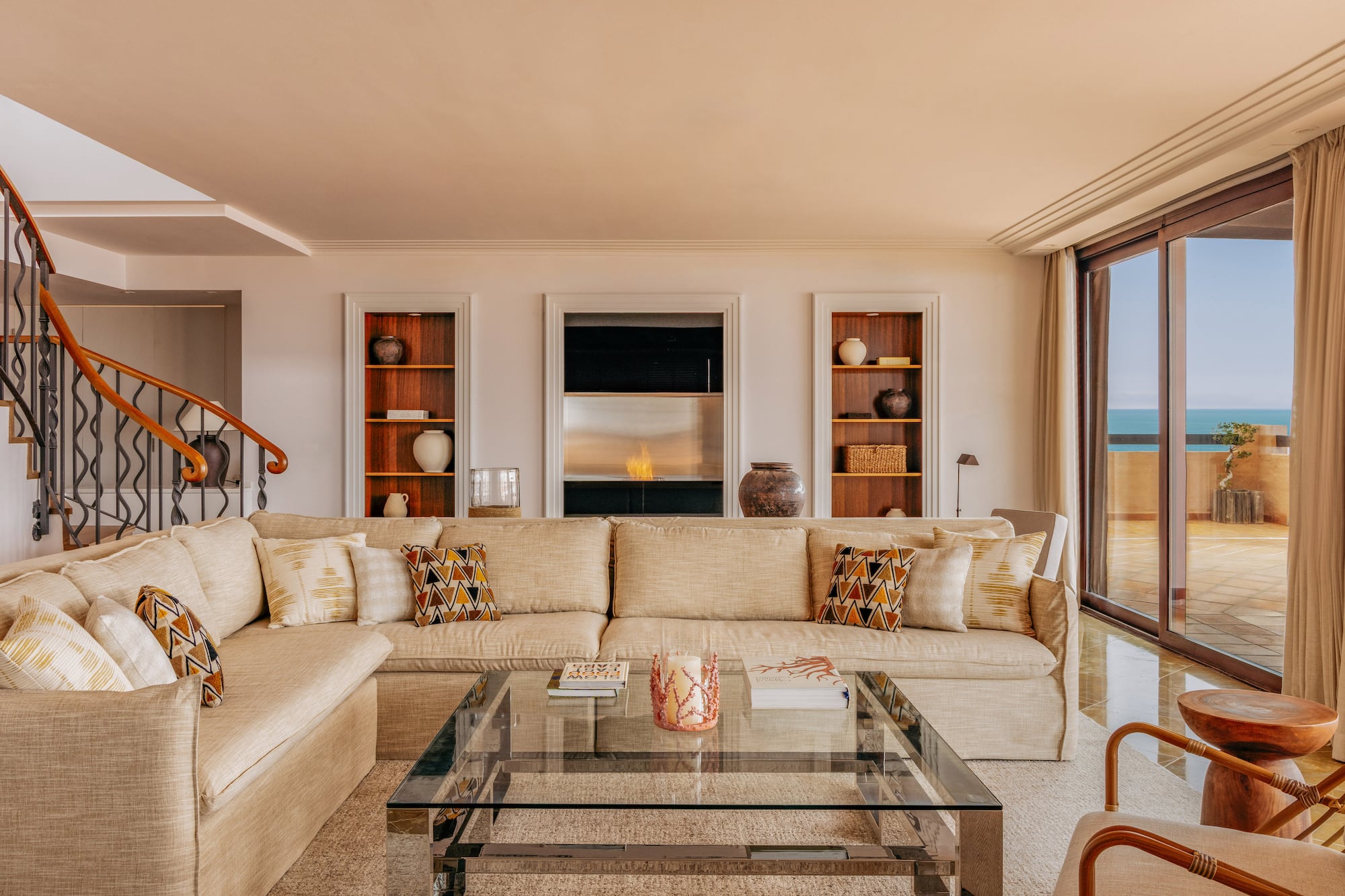 Spacious living room with beige sofa, modern fireplace, and ocean view balcony.