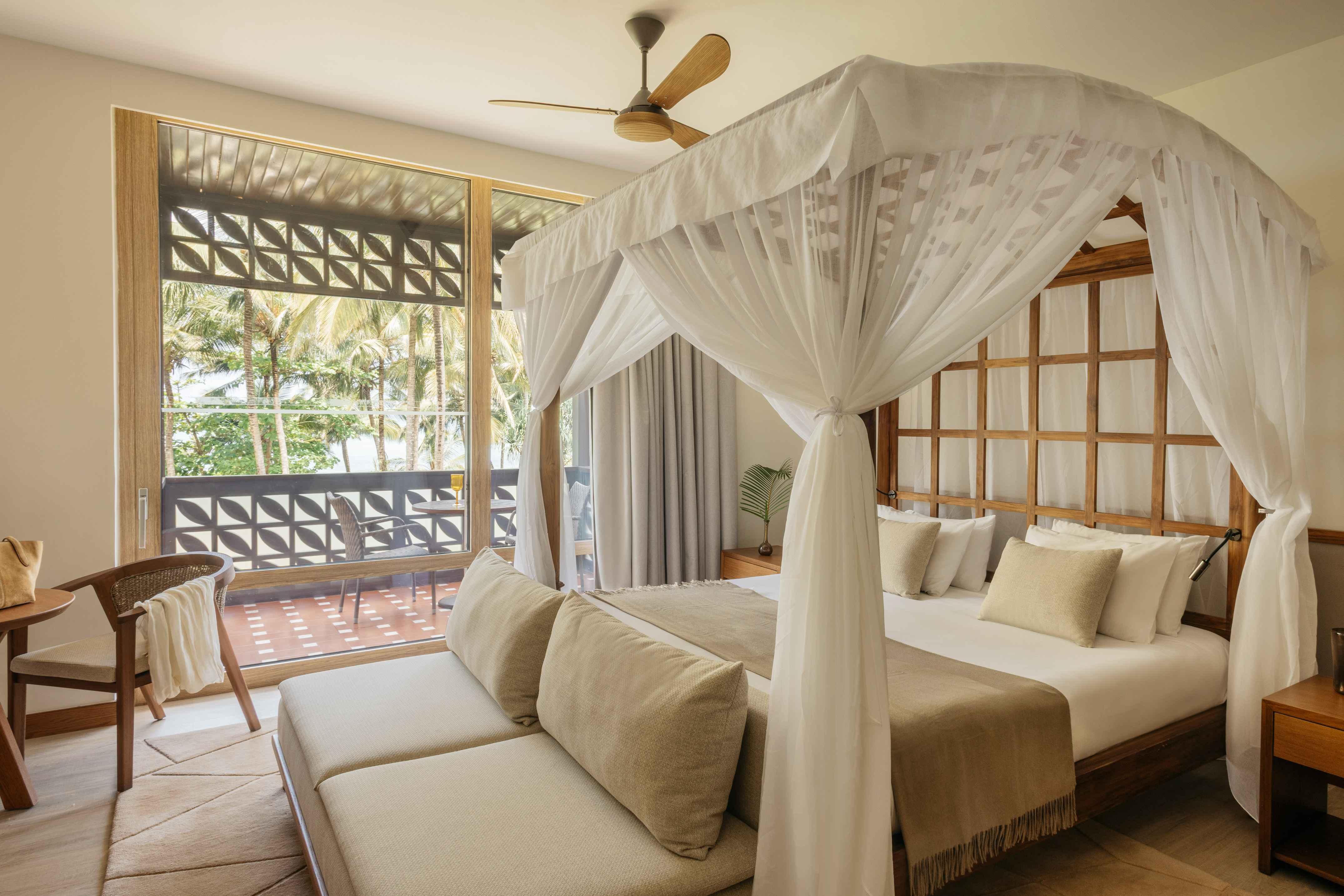 Luxury hotel bedroom with four-poster bed, balcony, and tropical view.