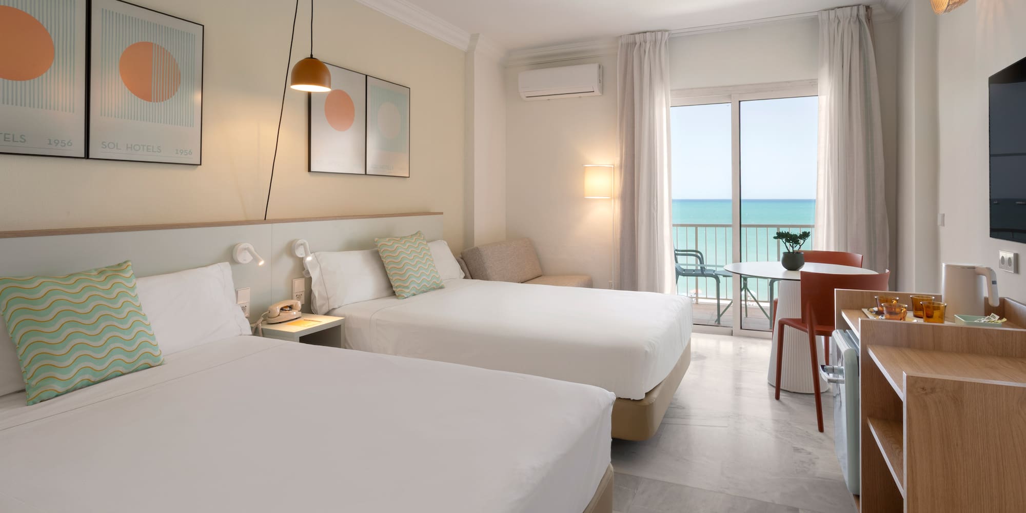 Habitación de hotel moderna con dos camas, balcón y vistas al mar.