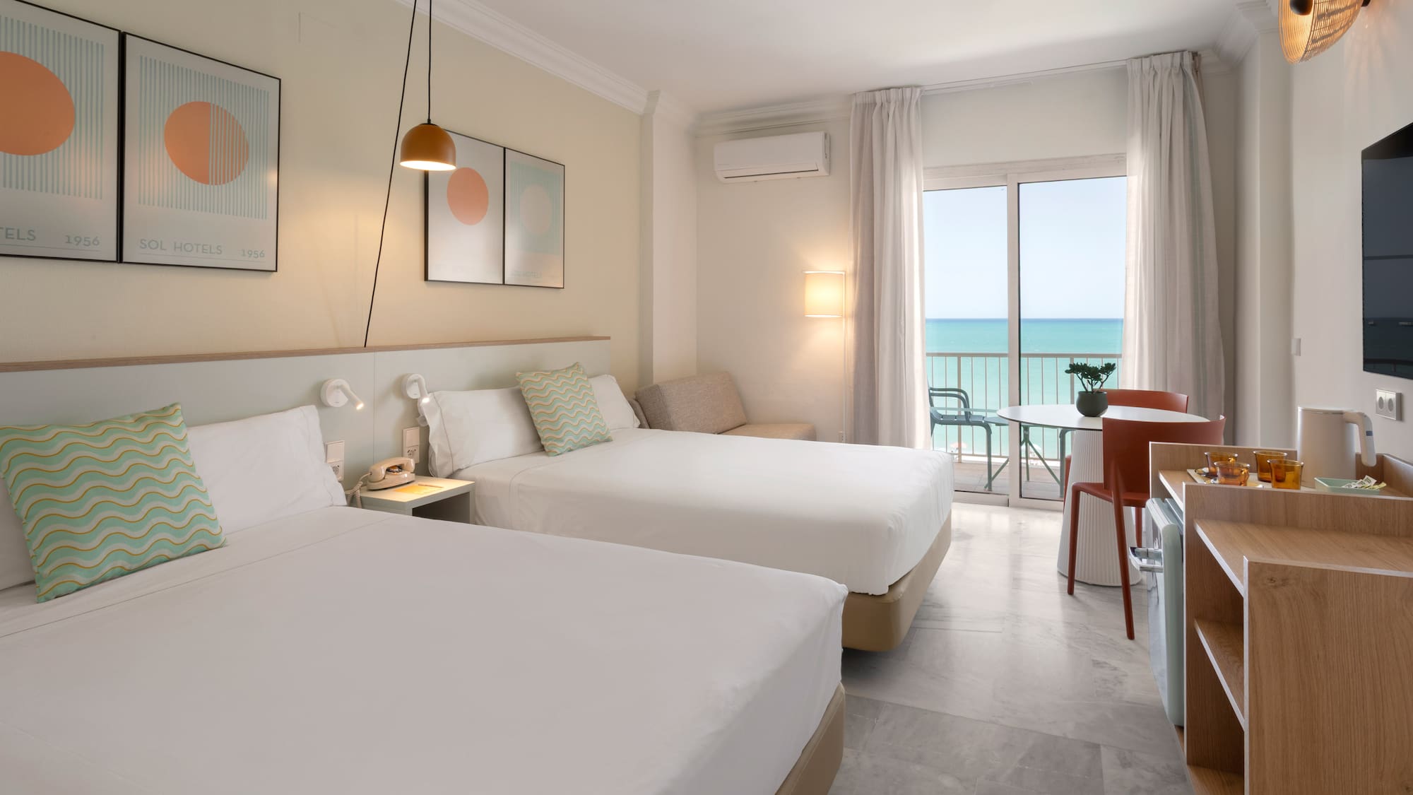 Habitación de hotel moderna con dos camas, balcón y vistas al mar.