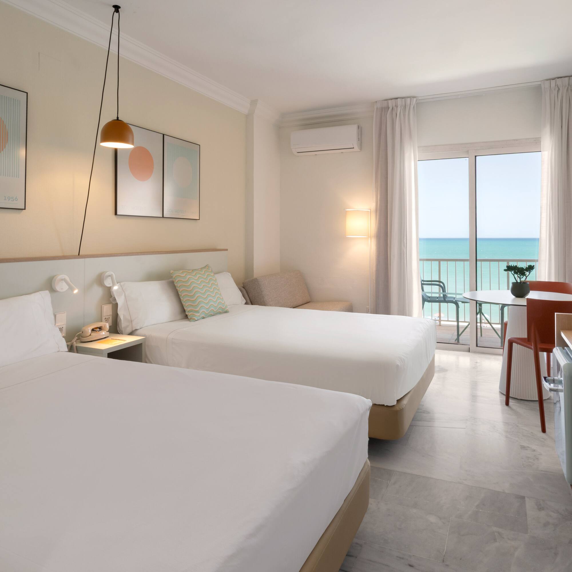 Habitación de hotel moderna con dos camas, balcón y vistas al mar.