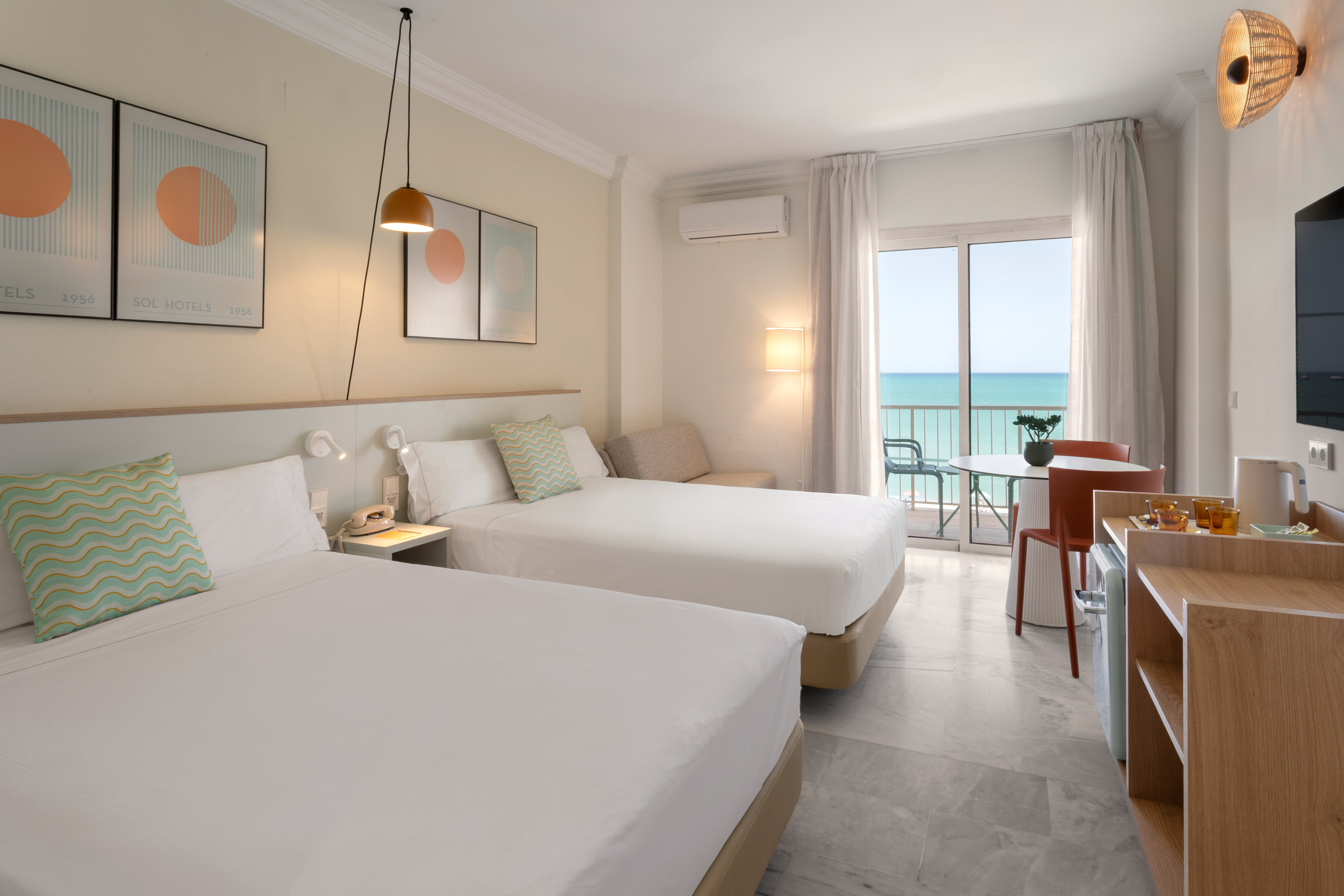 Habitación de hotel moderna con dos camas, balcón y vistas al mar.