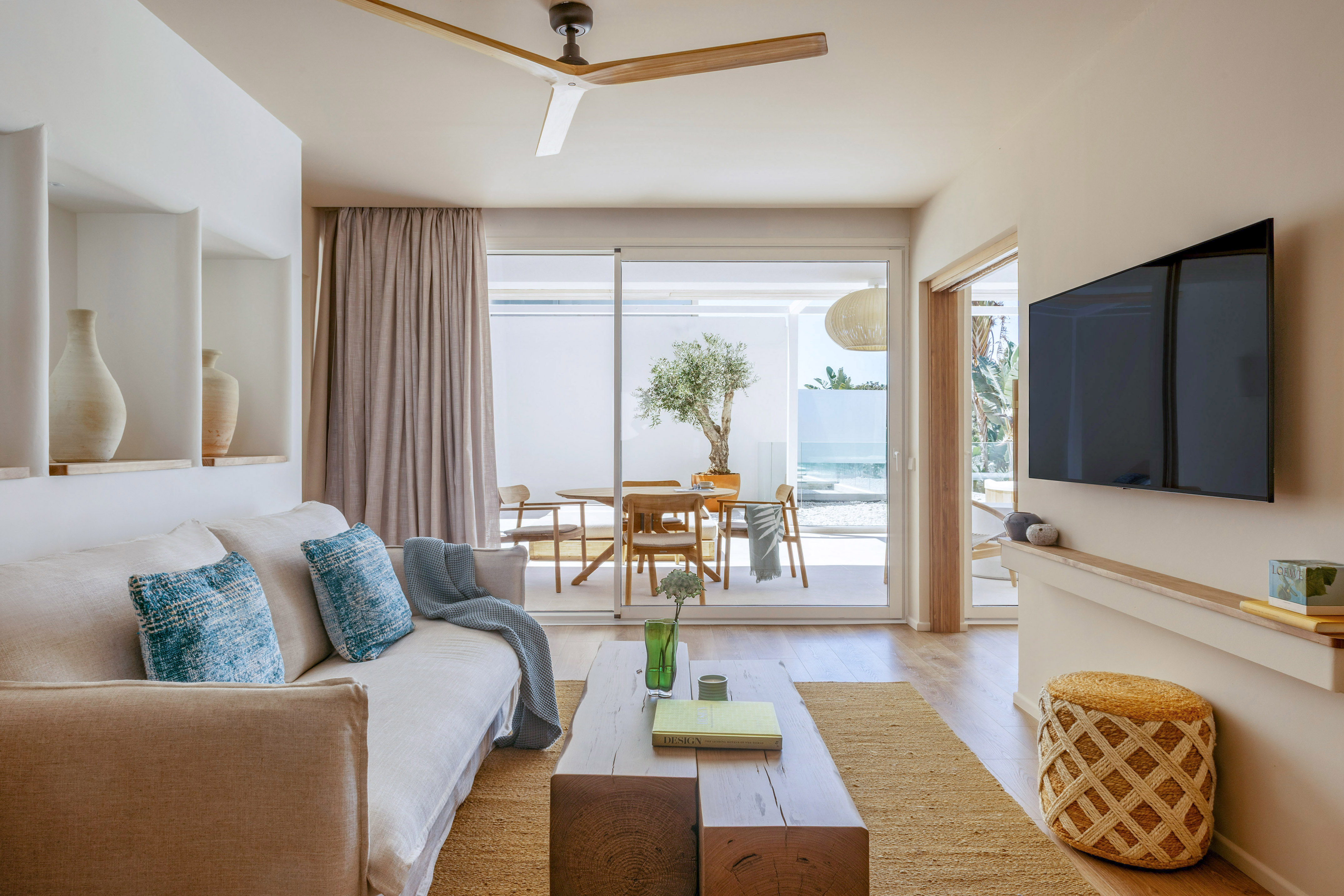 Modern living room with natural wood elements, neutral sofa, and patio dining.