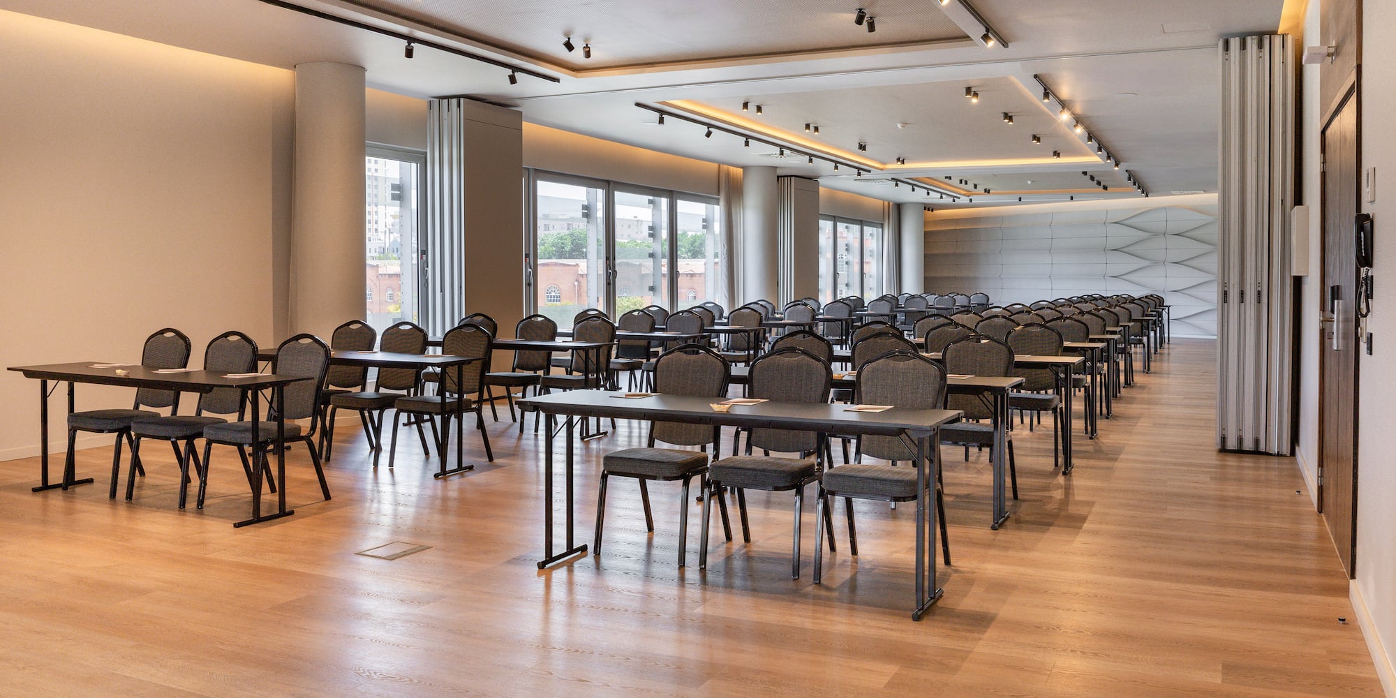 Modern empty conference room with rows of tables, chairs, and large windows.