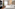 Modern hotel bedroom with white bed, large window, TV, and potted plant.