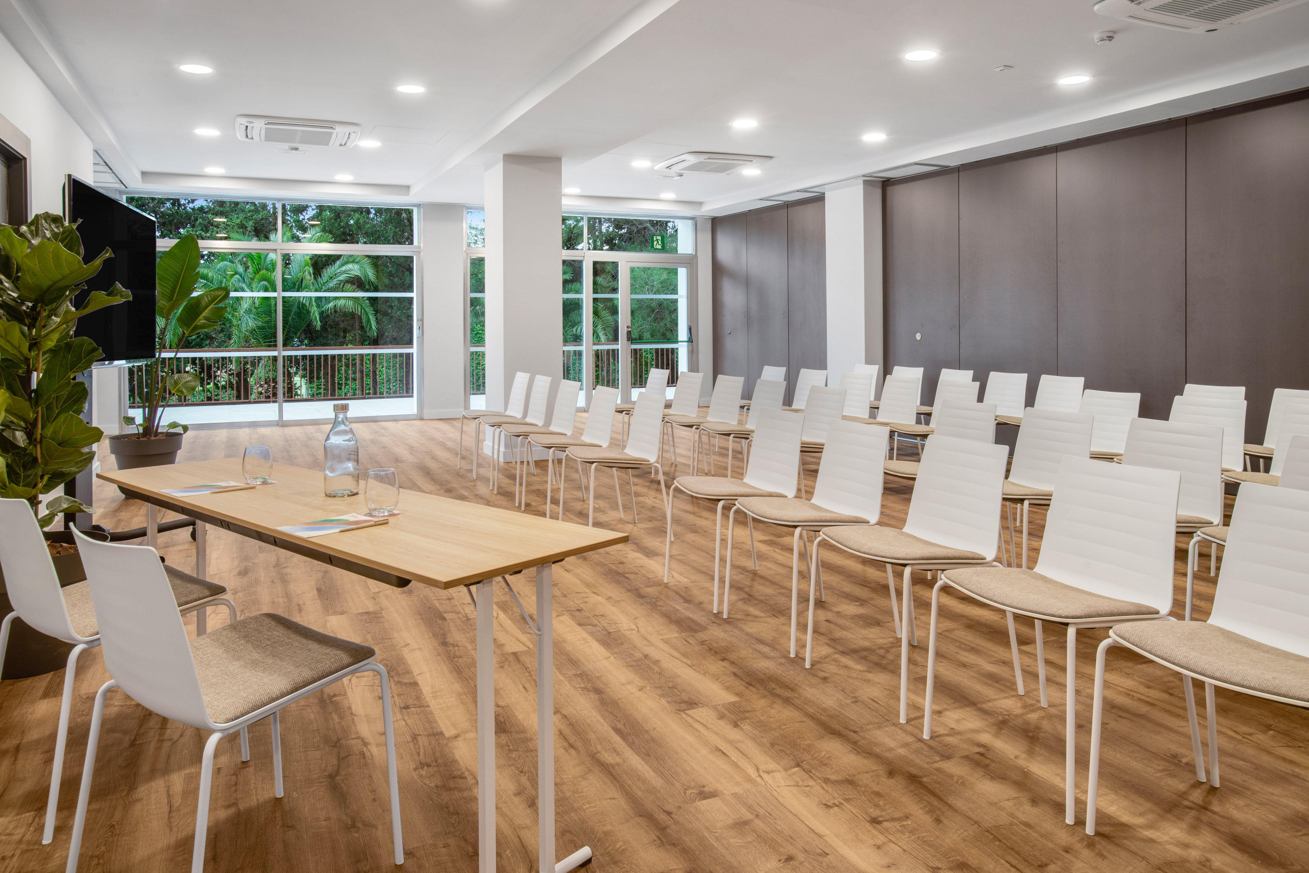 Modern meeting room with chairs, presentation table, and tropical view.