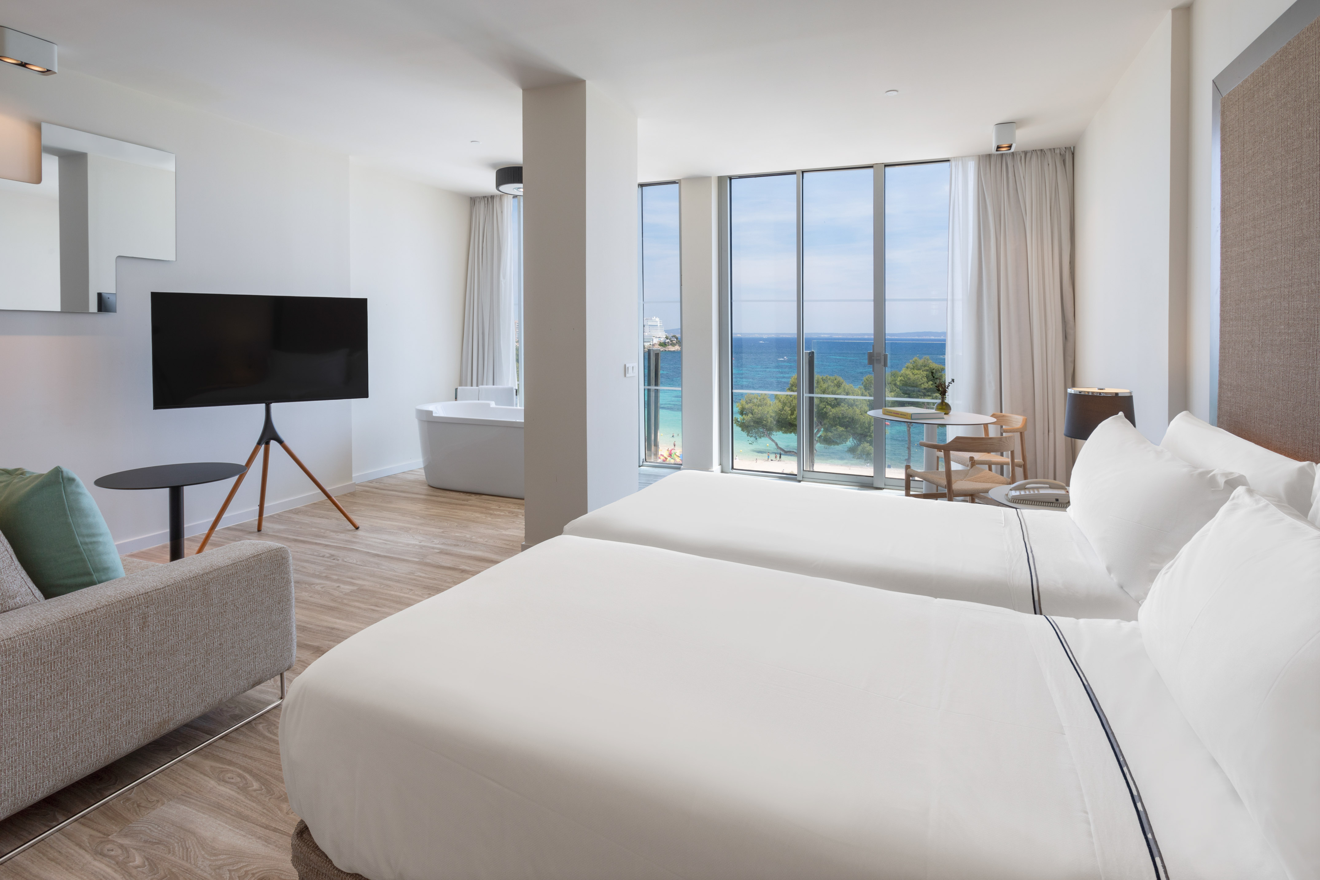 Modern hotel room with twin beds, ocean view, beachfront, and freestanding tub.
