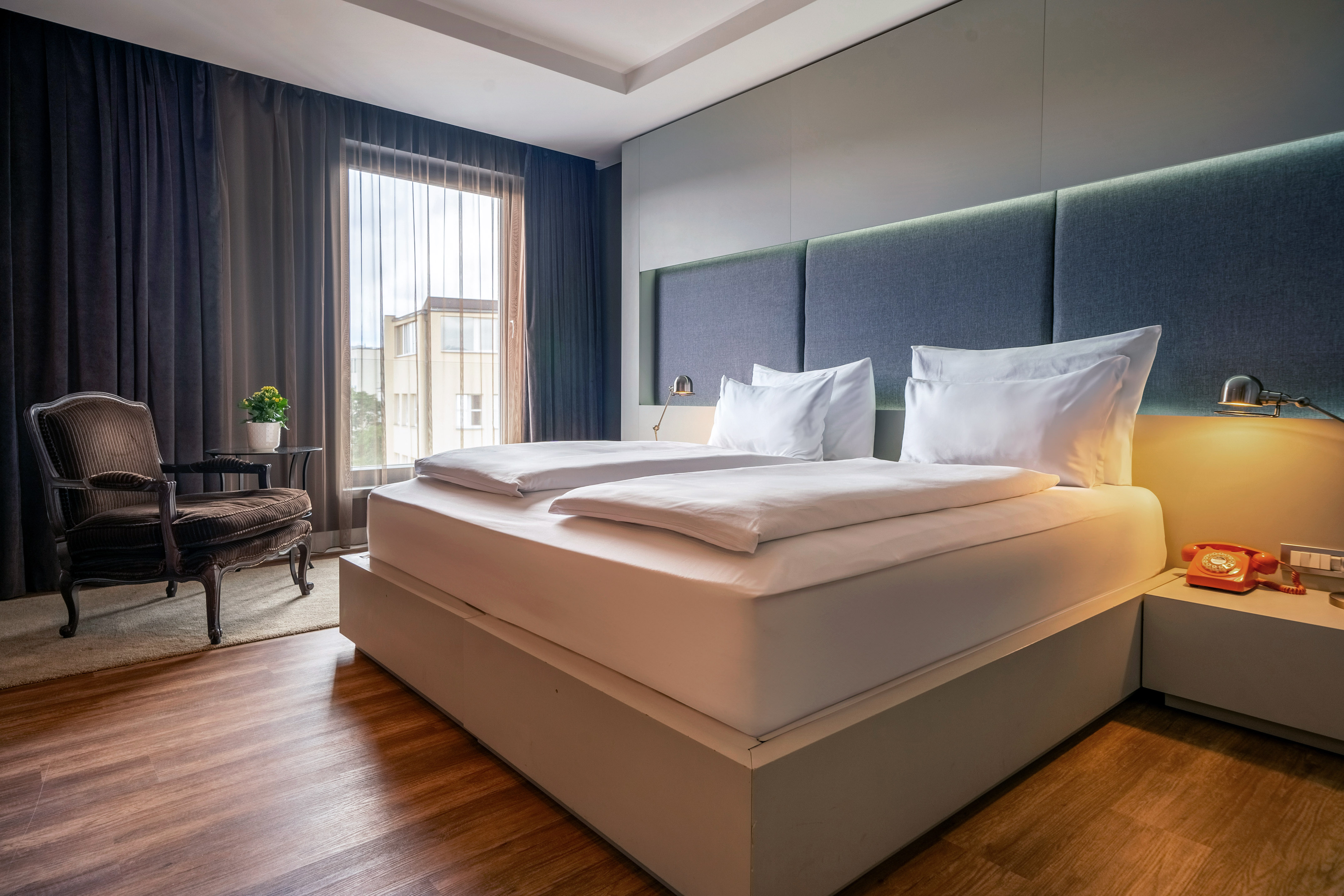 Stylish hotel room featuring a large bed, blue headboard, and cozy armchair.