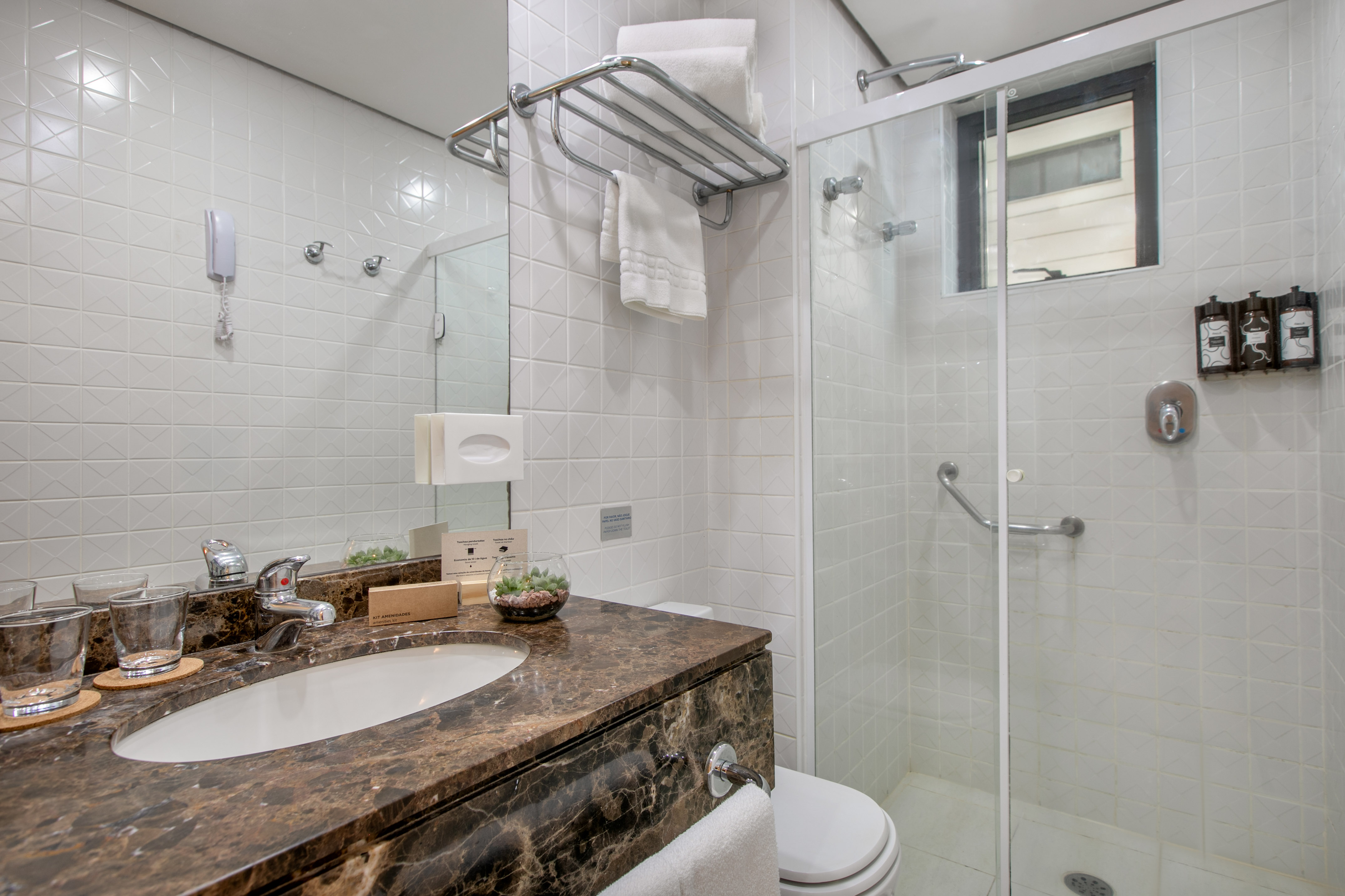 Modern hotel bathroom, white tiled walls, marble vanity, sink, glass shower.
