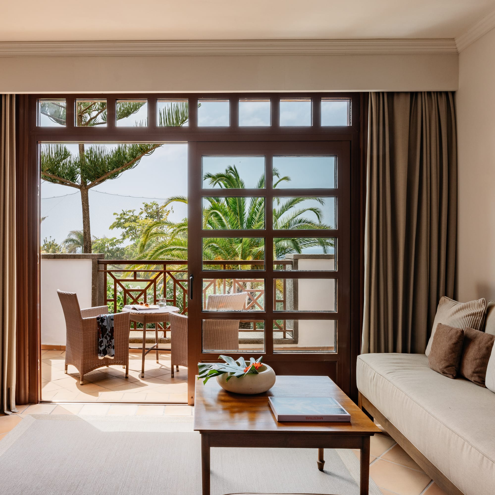 Living room with balcony, outdoor seating, and tropical palm tree view.