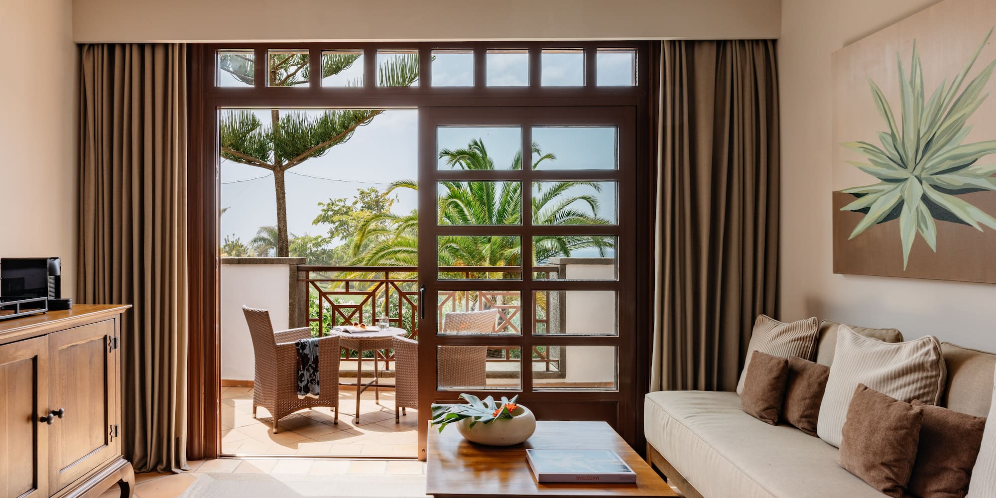 Living room with balcony, outdoor seating, and tropical palm tree view.