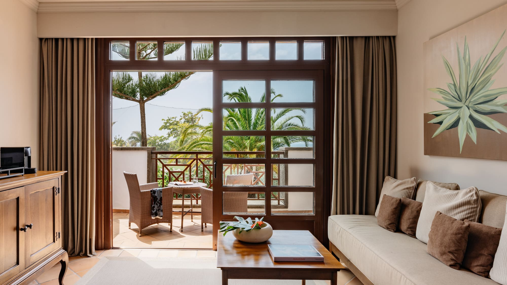Living room with balcony, outdoor seating, and tropical palm tree view.