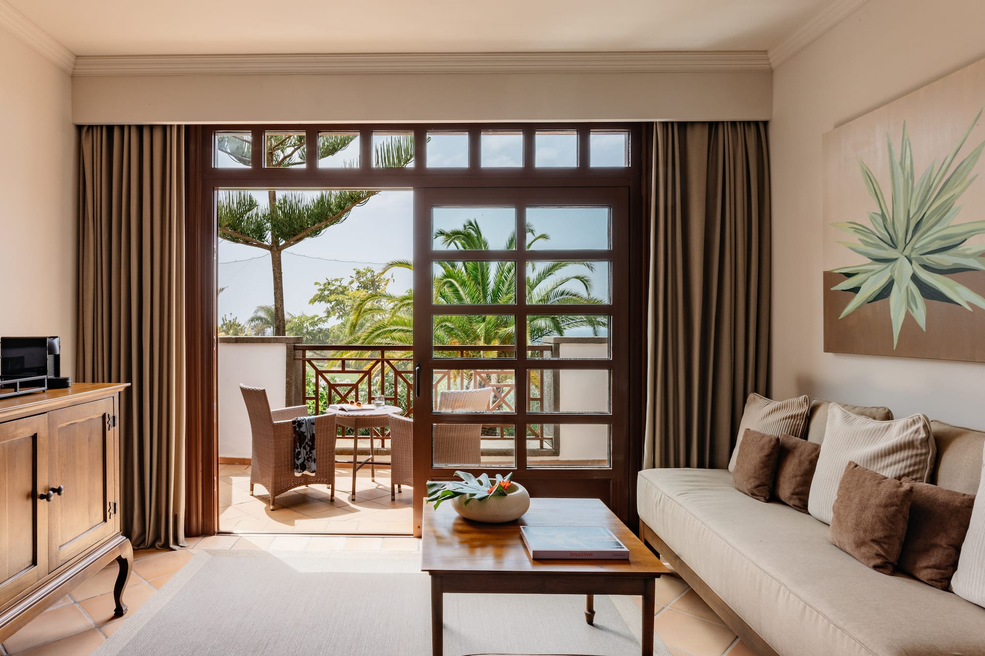 Living room with balcony, outdoor seating, and tropical palm tree view.