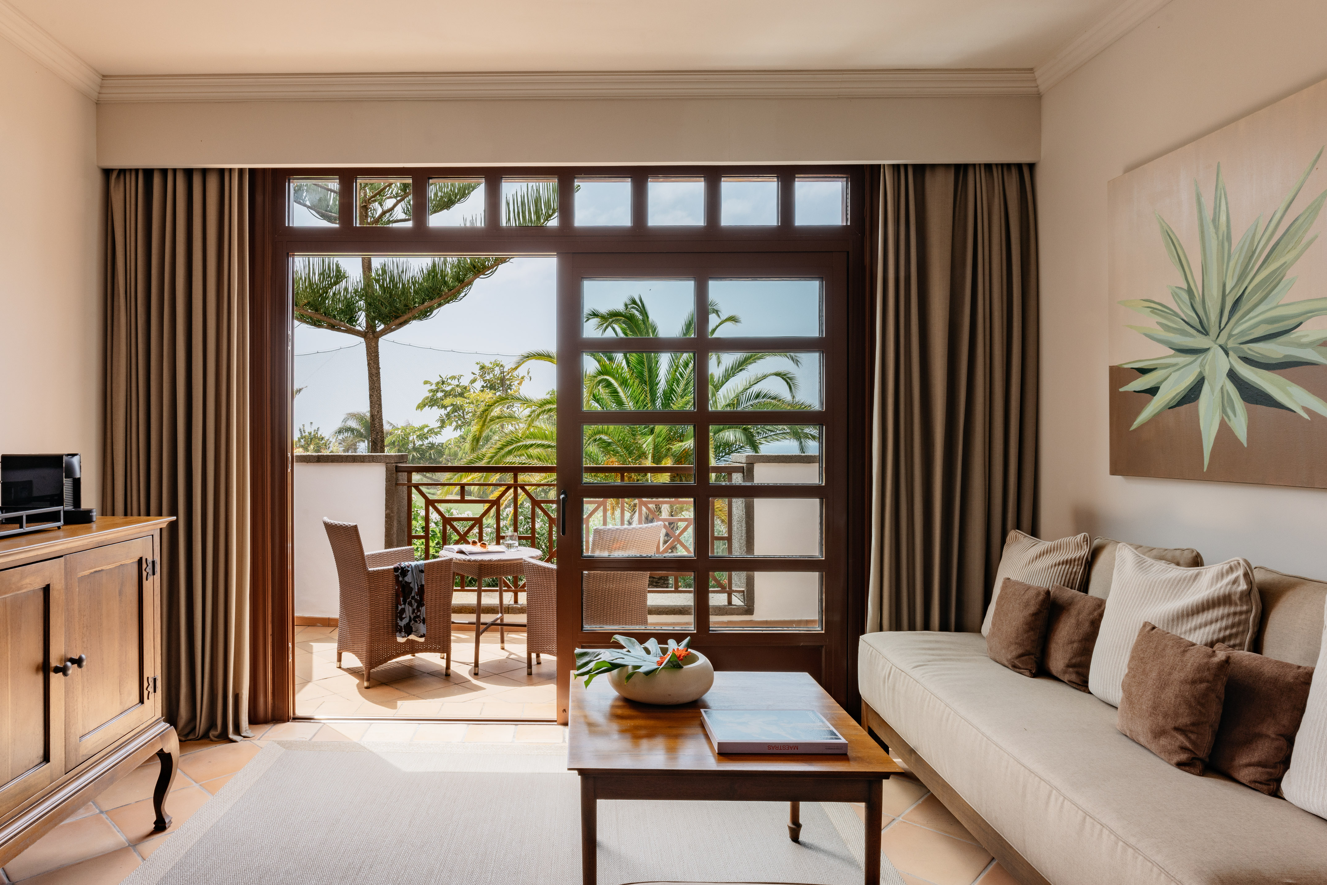 Living room with balcony, outdoor seating, and tropical palm tree view.