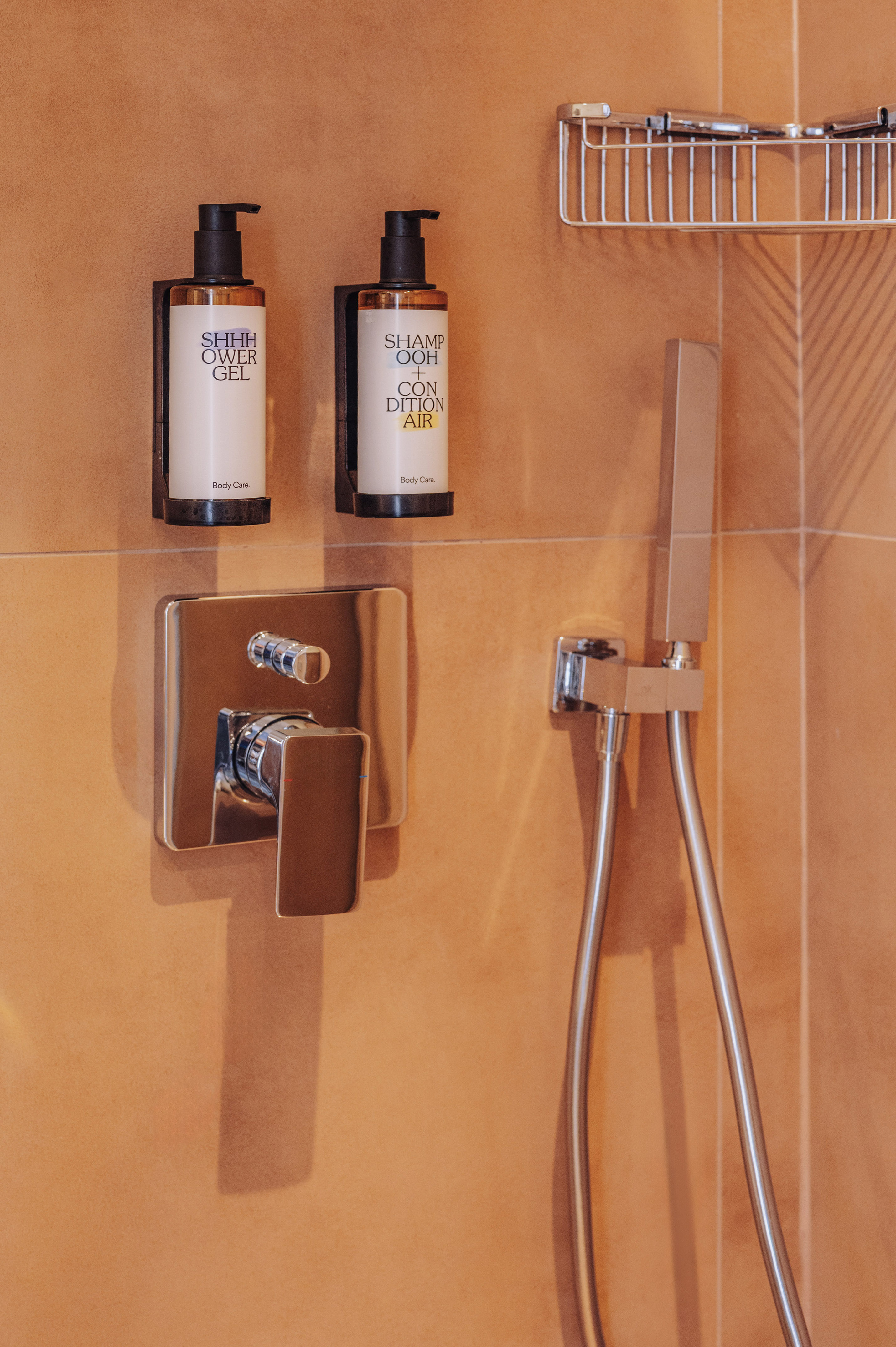 Hotel shower with mounted shampoo, conditioner, shower gel, and chrome fixtures.