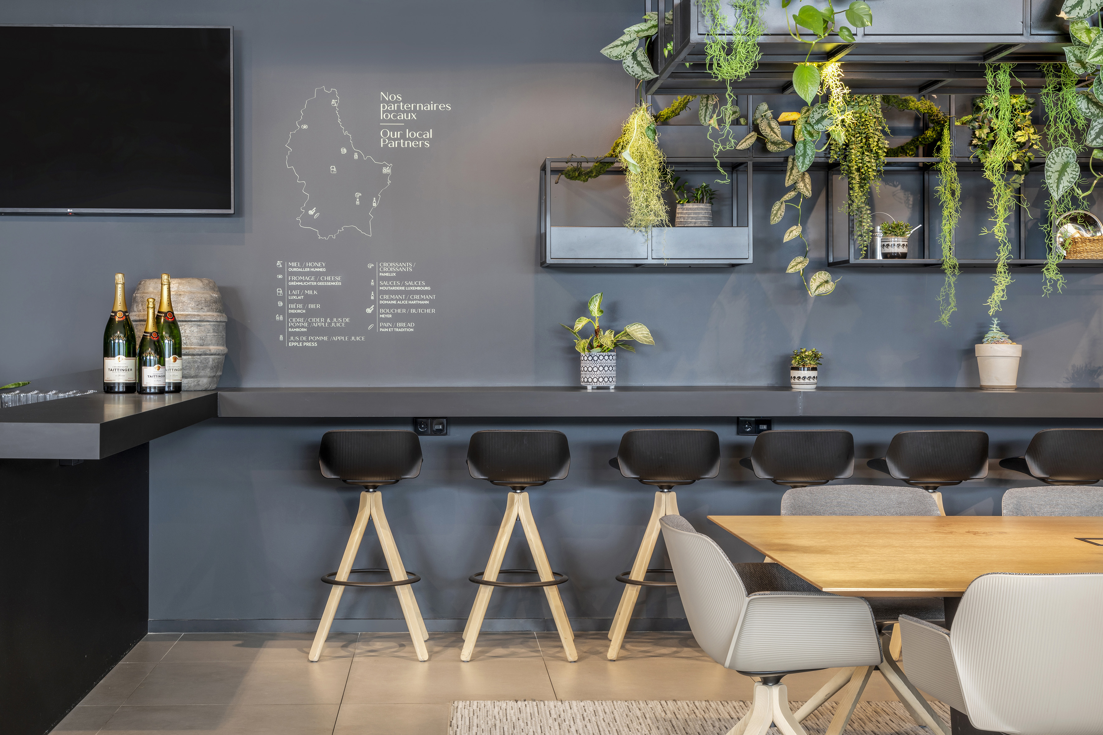 Modern bar counter with Taittinger champagne, bar stools, local partner wall, and green plants. - De Gaart, Cuisine locale - INNSiDE Luxembourg, Luxembourg