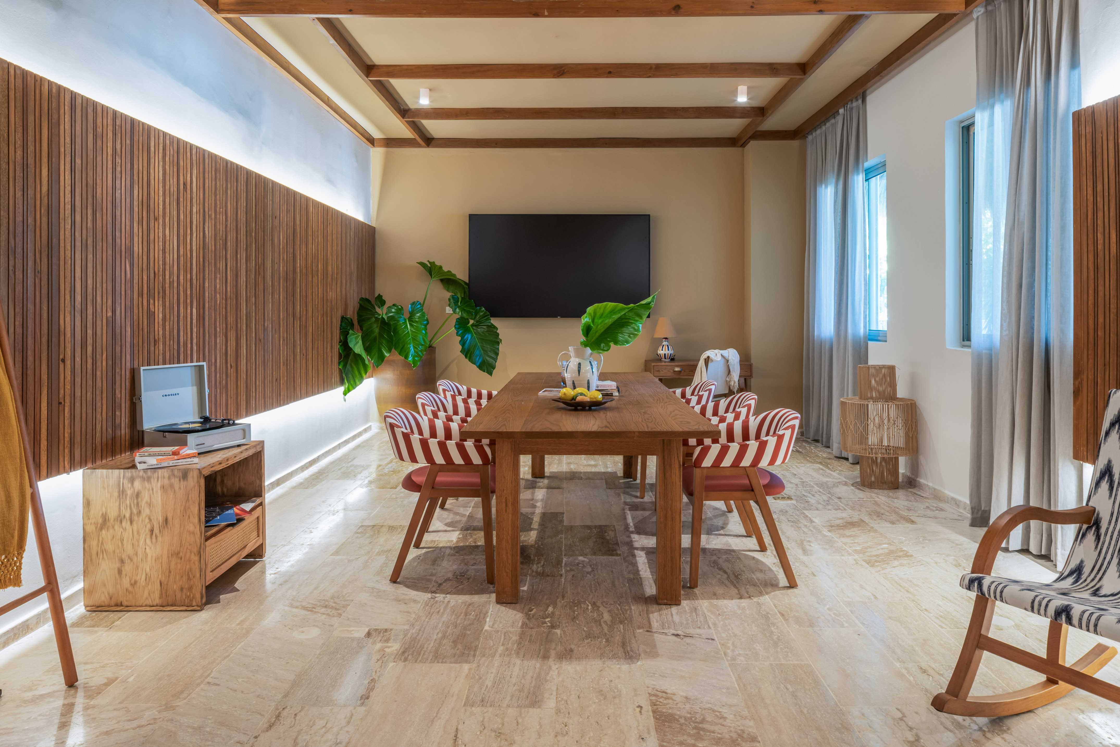 Modern dining room: wooden table, red striped chairs, wood paneling, plants.