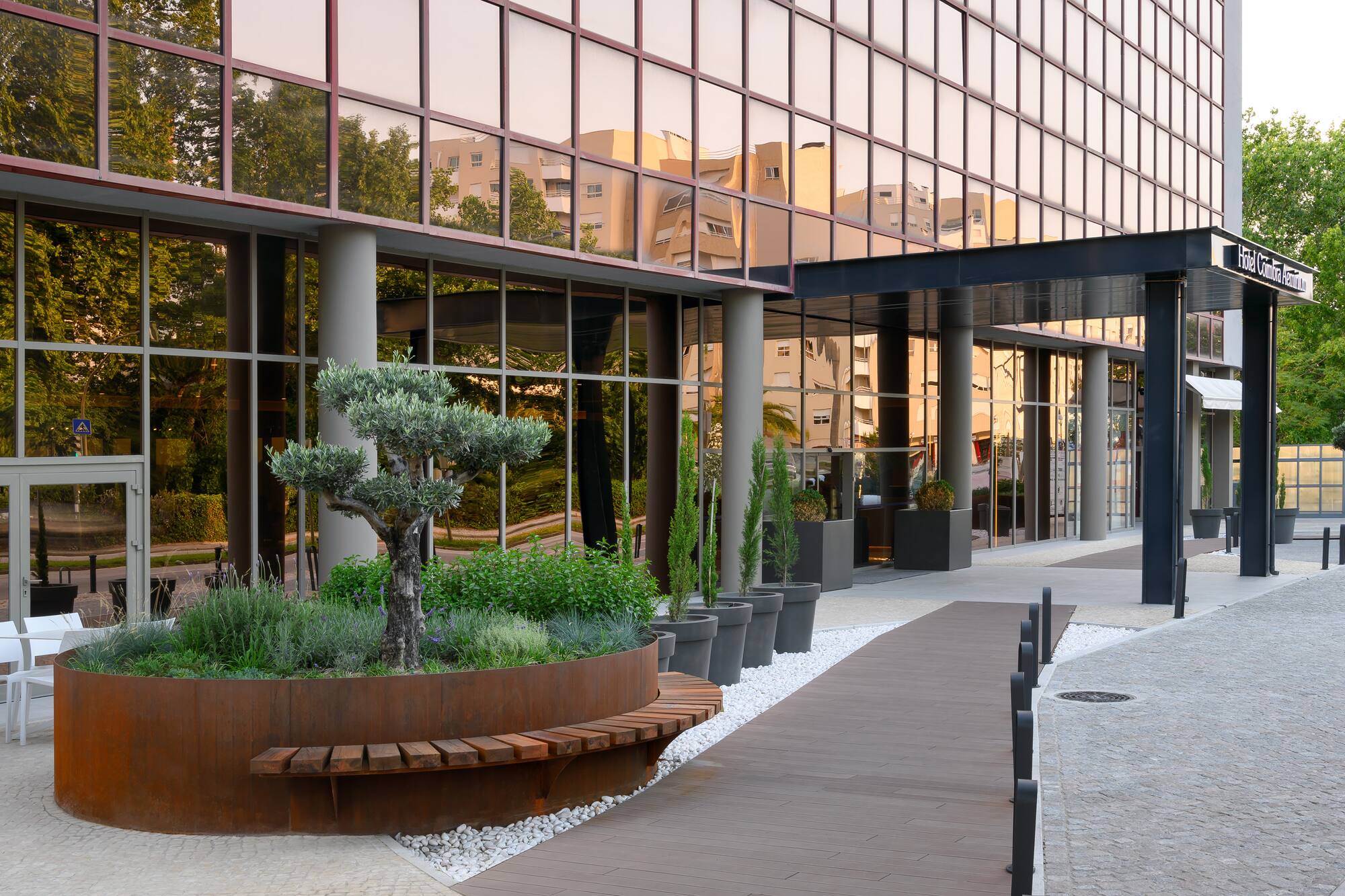 Modern hotel entrance, glass facade, Corten steel planter with olive tree.