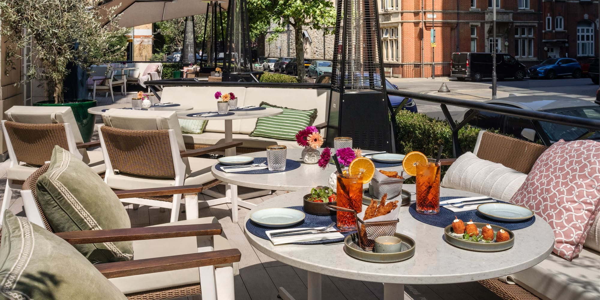 Outdoor dining patio with appetizers, cocktails, umbrellas, and urban view.