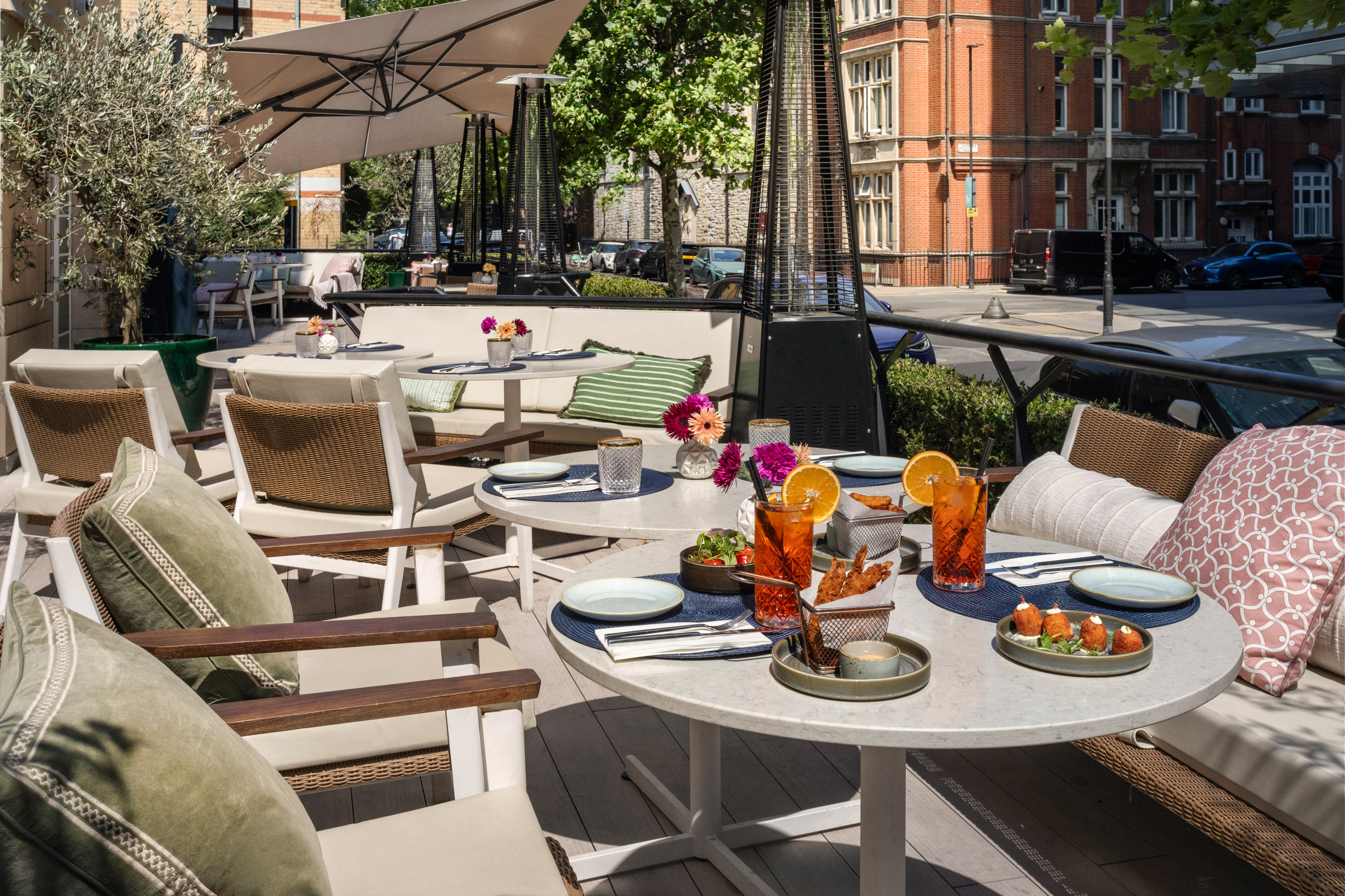 Outdoor dining patio with appetizers, cocktails, umbrellas, and urban view.
