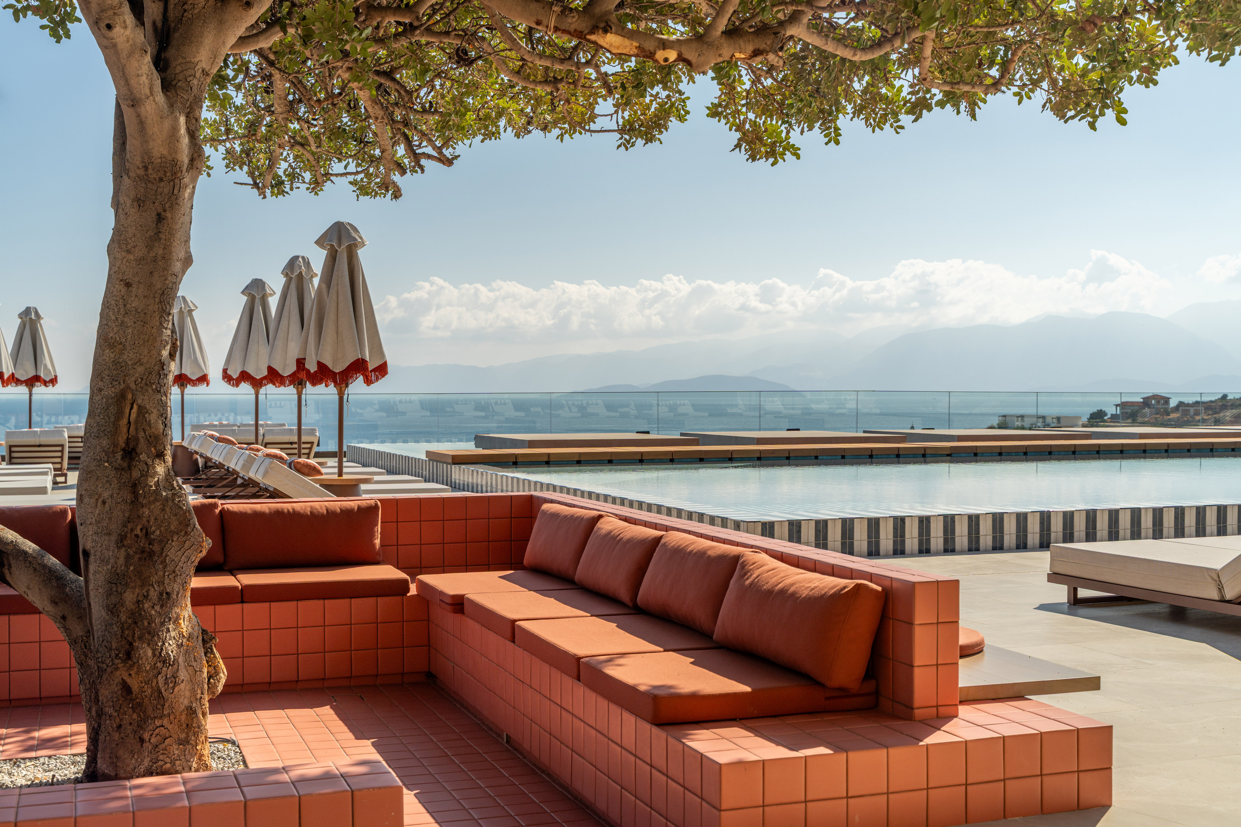Shaded outdoor lounge with orange seating, infinity pool, and ocean view.