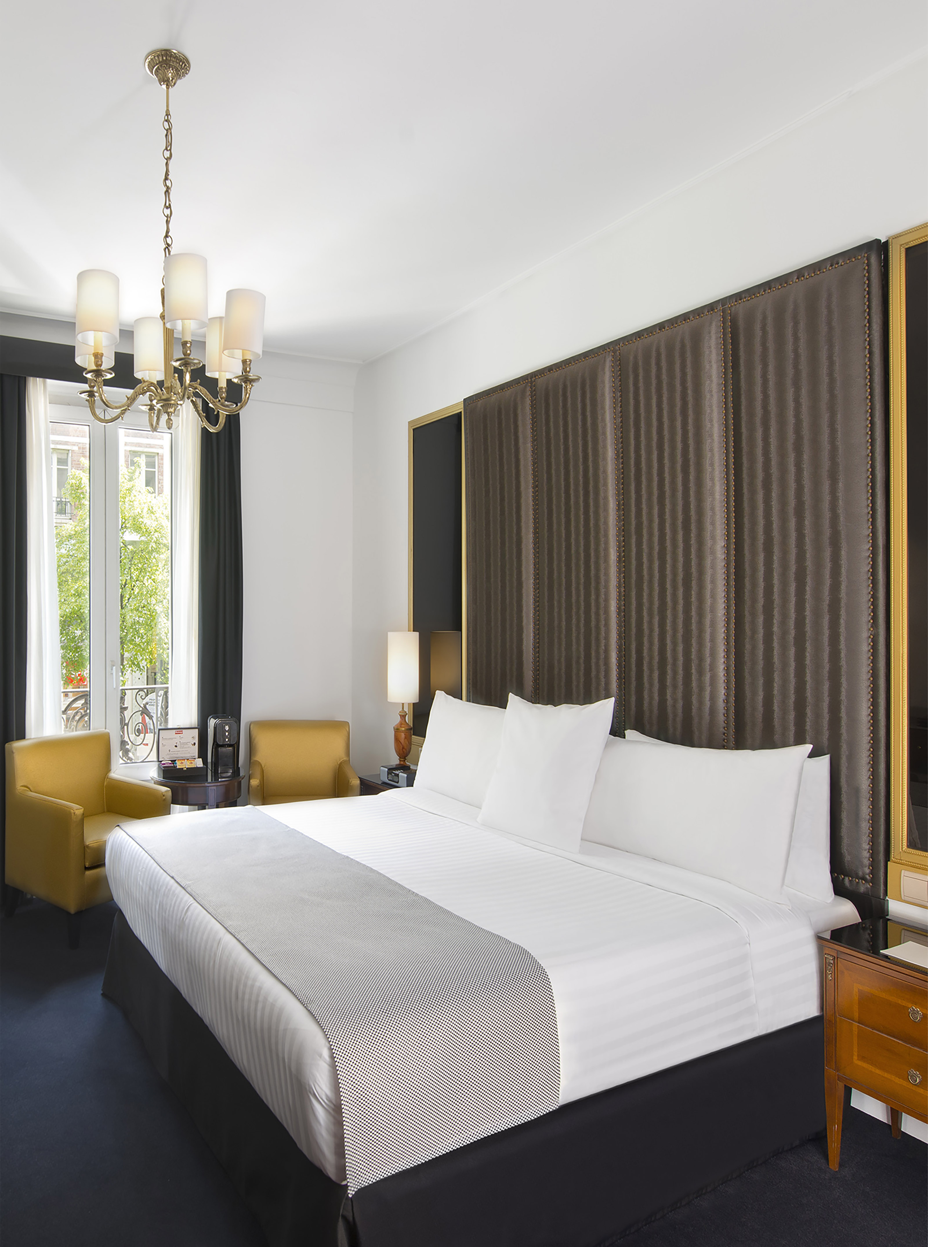 Luxury hotel room with king bed, dark tufted headboard, yellow armchairs.