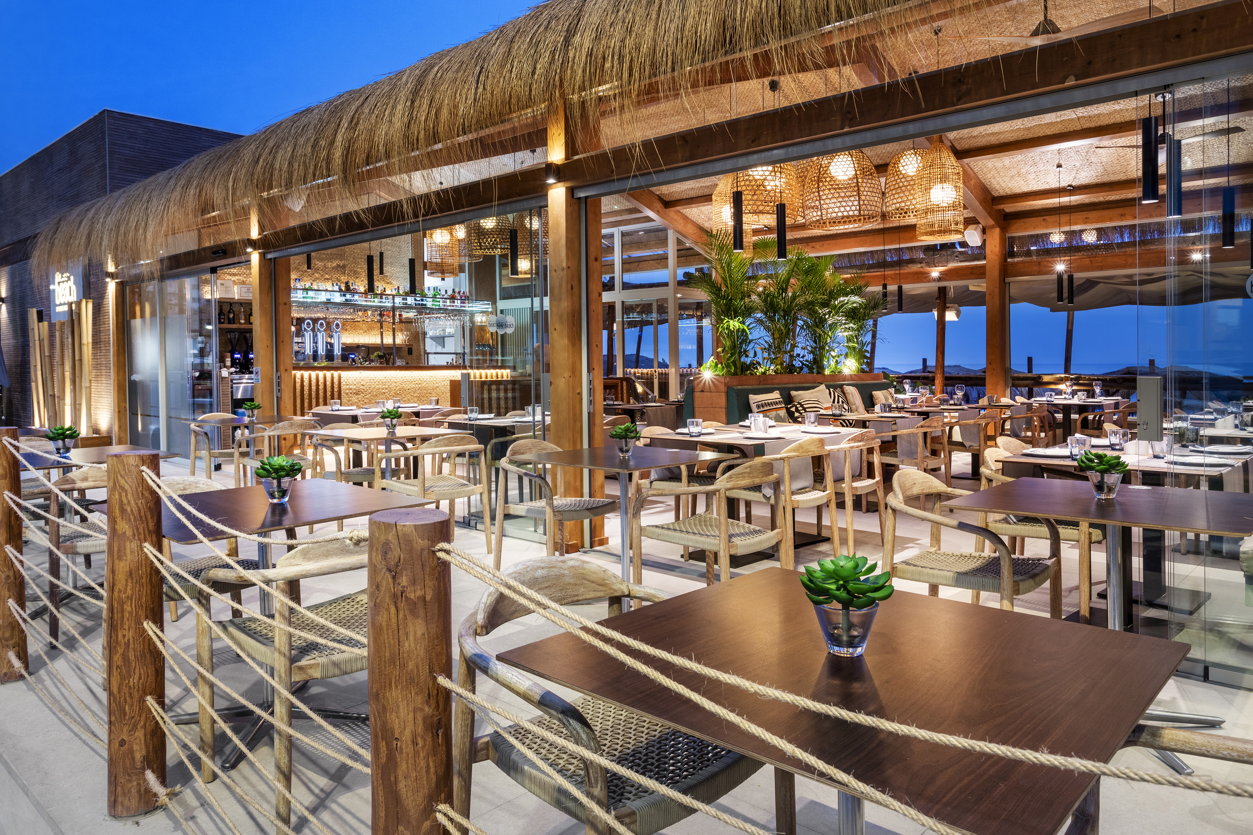 Beachfront restaurant with thatched roof, outdoor dining, and illuminated bar.