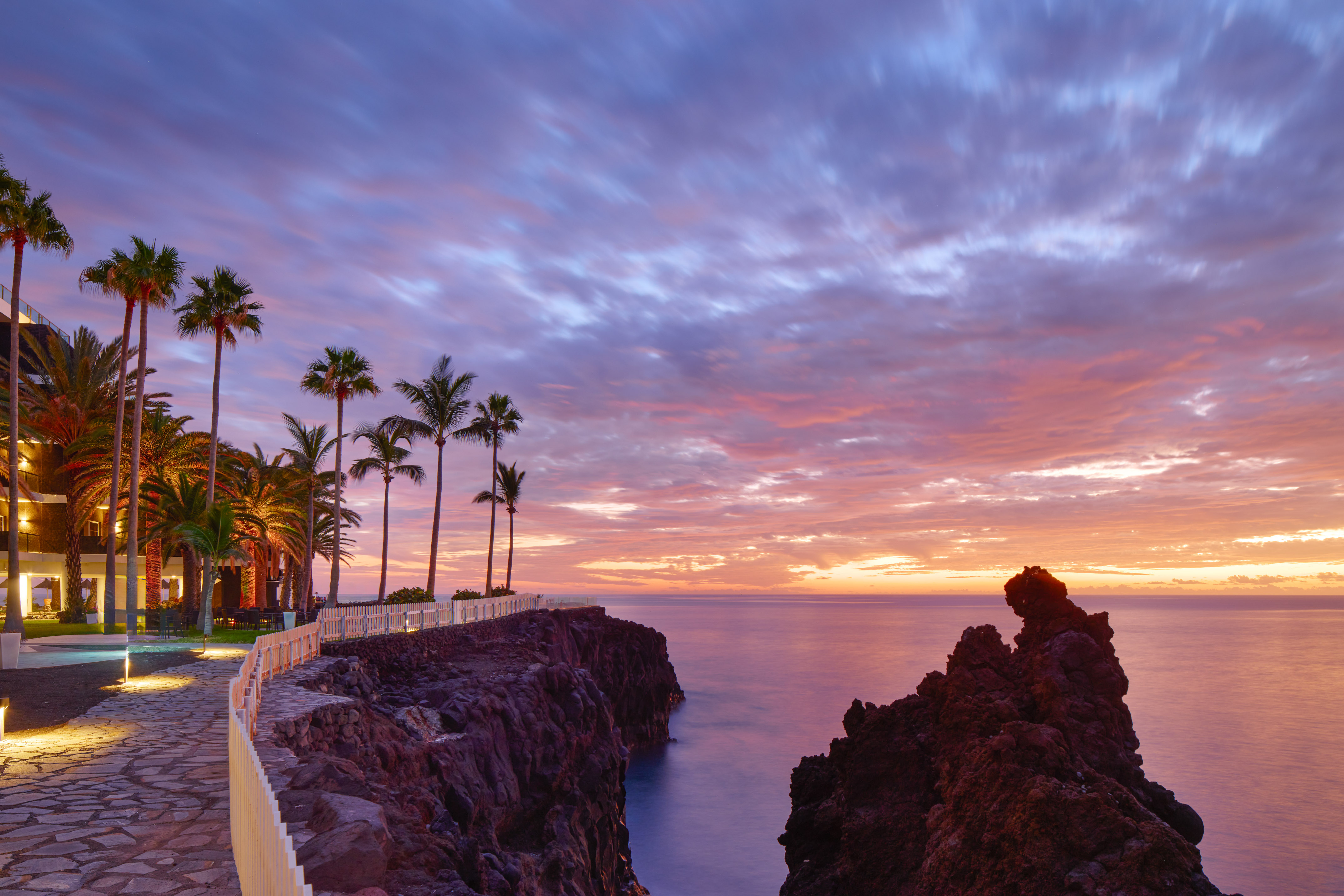 Coastal resort path at vibrant sunset with palm trees and ocean.