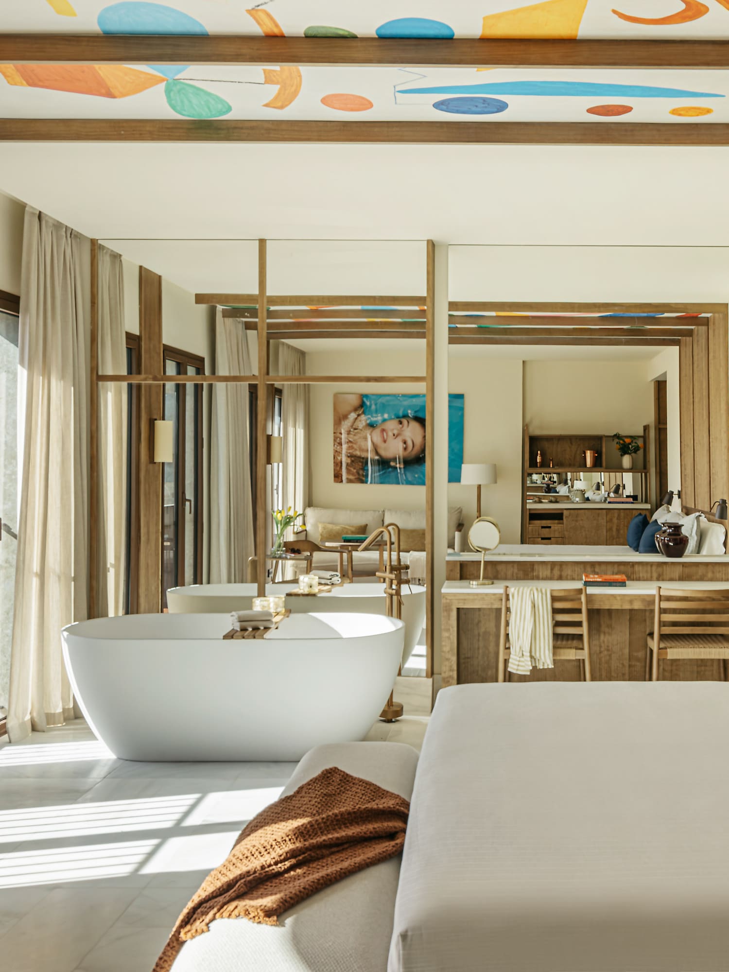 Luxury hotel suite with freestanding tub, modern bed, and colorful ceiling art.