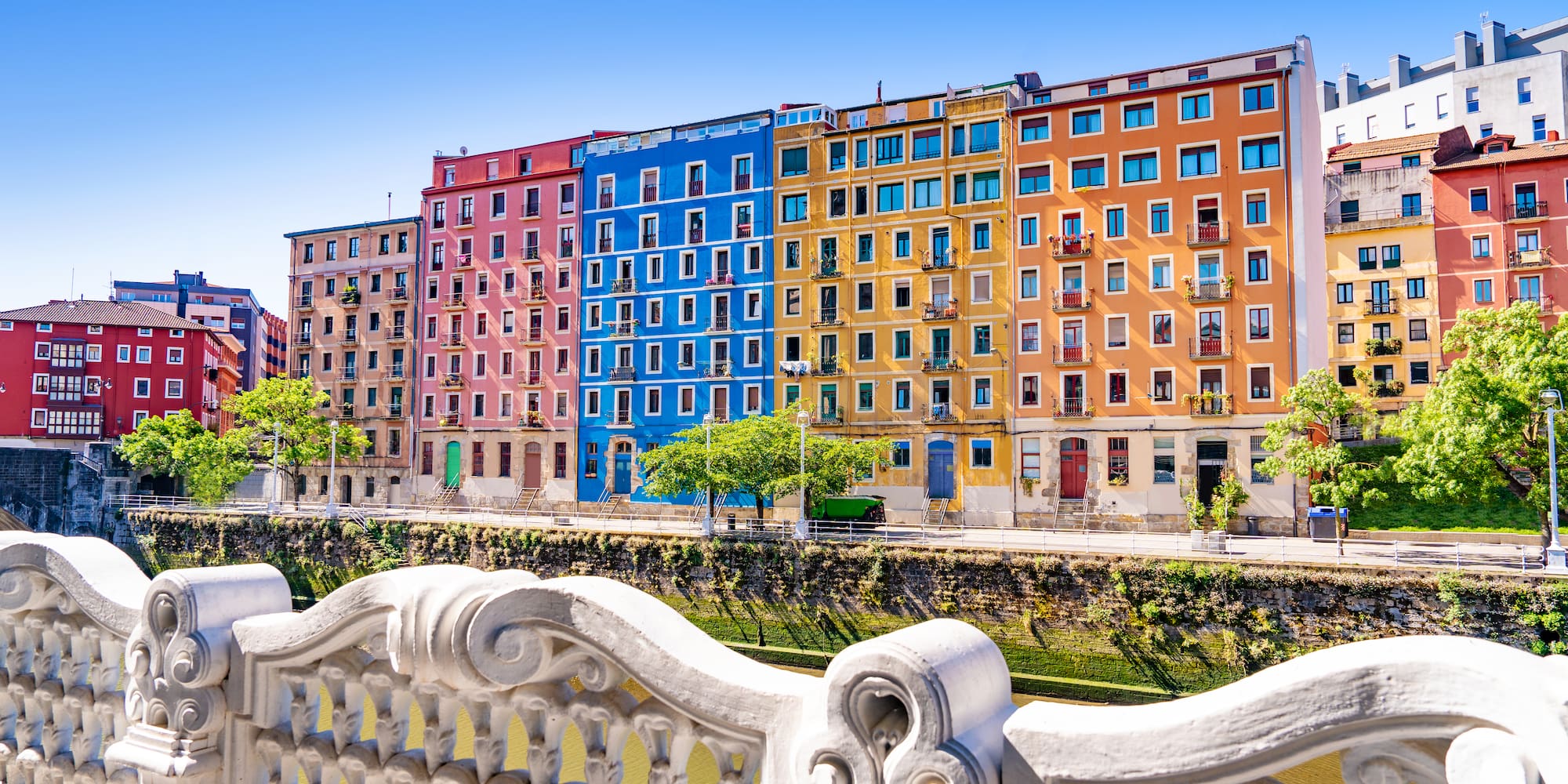 Colorful riverside buildings and ornate white bridge railing.