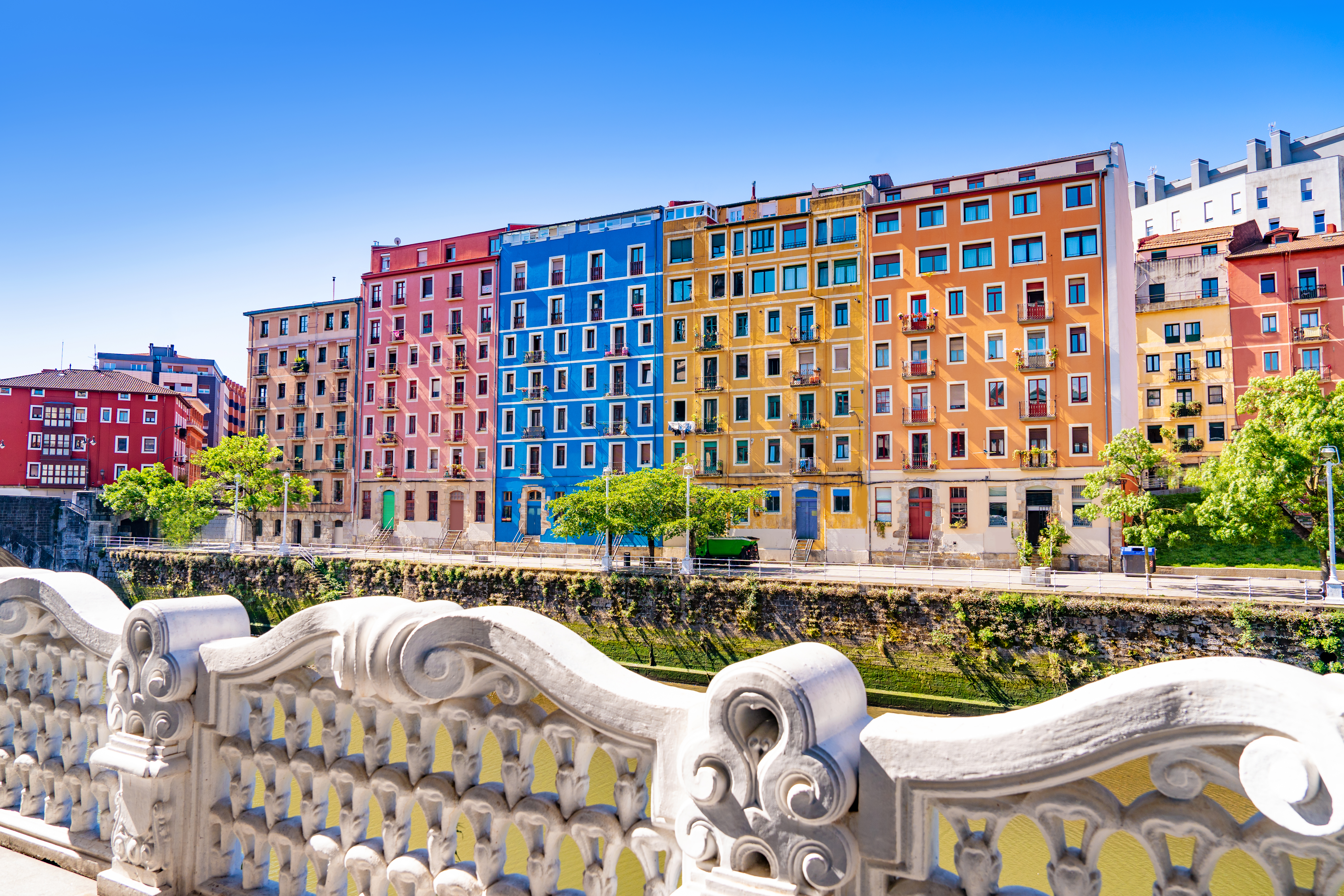 Colorful riverside buildings and ornate white bridge railing.