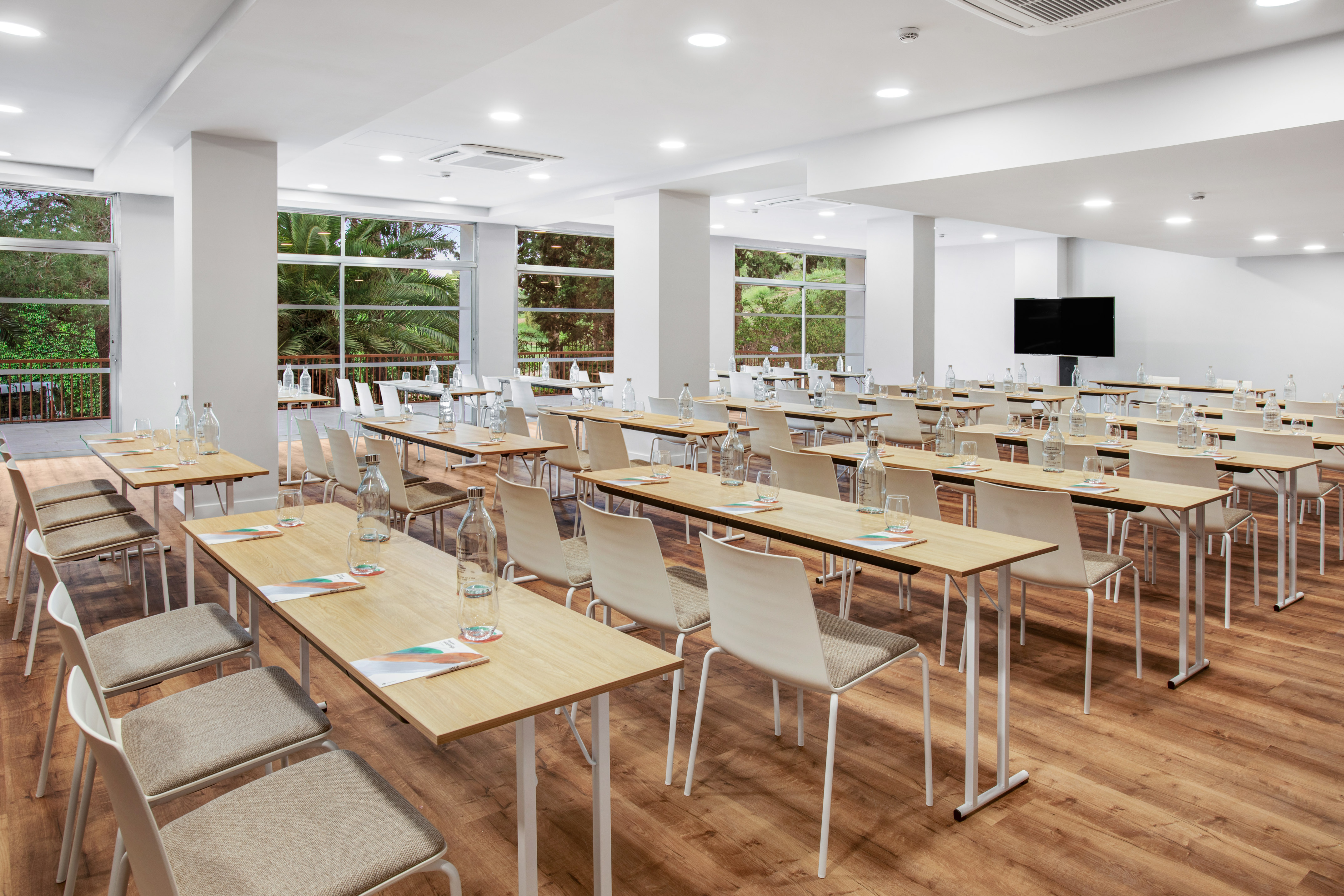 Modern conference room with tables, chairs, large windows, and a screen.