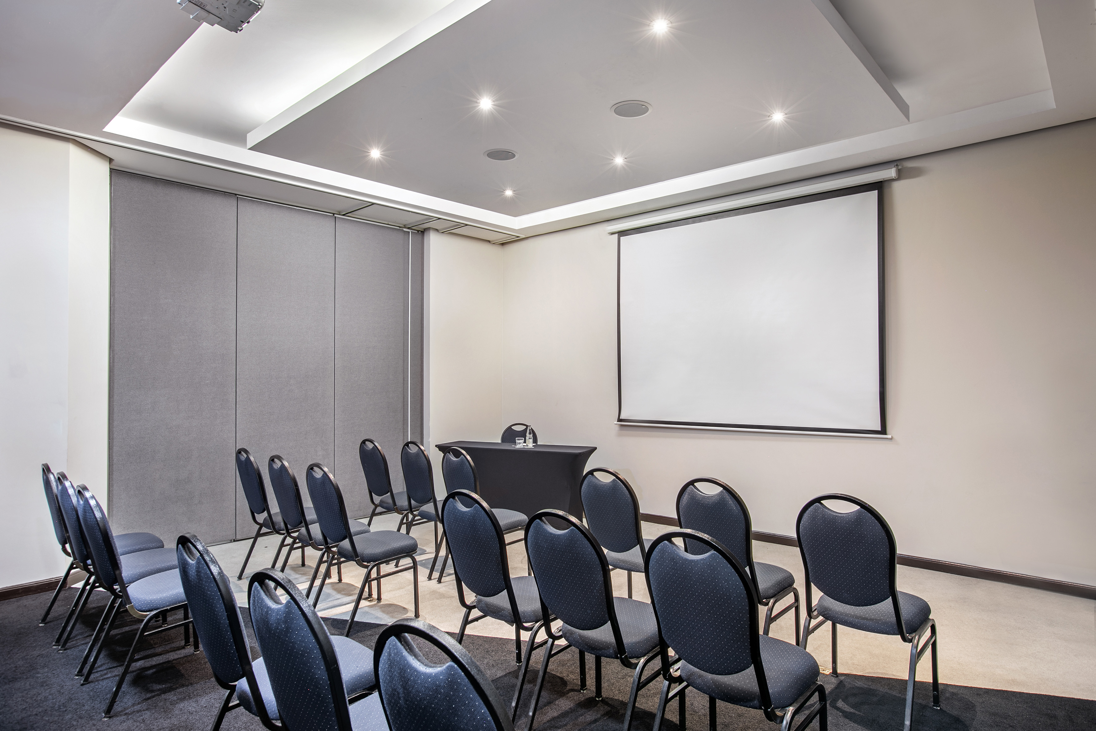Modern conference room with blue chairs, large projector screen, and small front table.