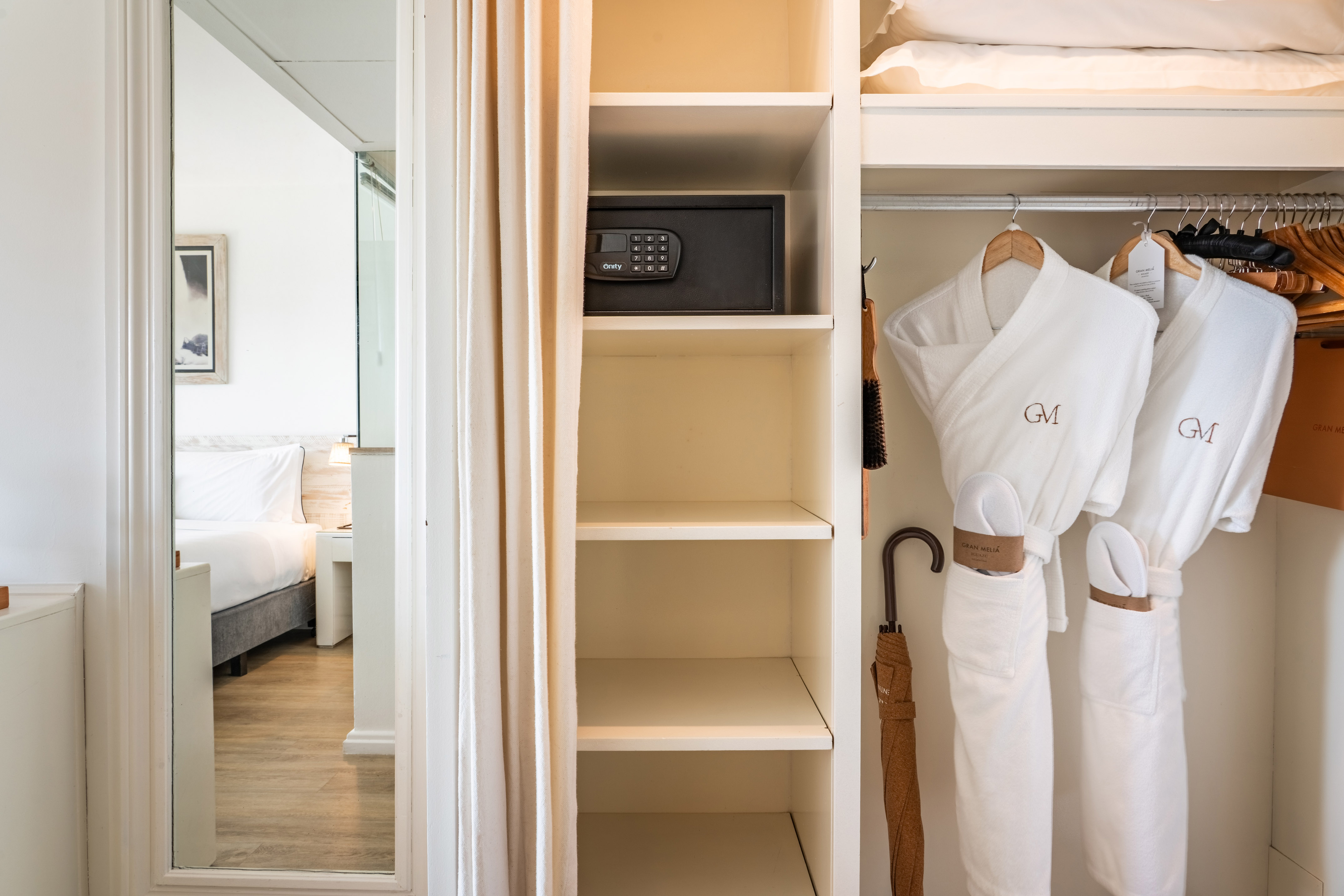 Hotel wardrobe with white bathrobes, in-room safe, and bedroom view.
