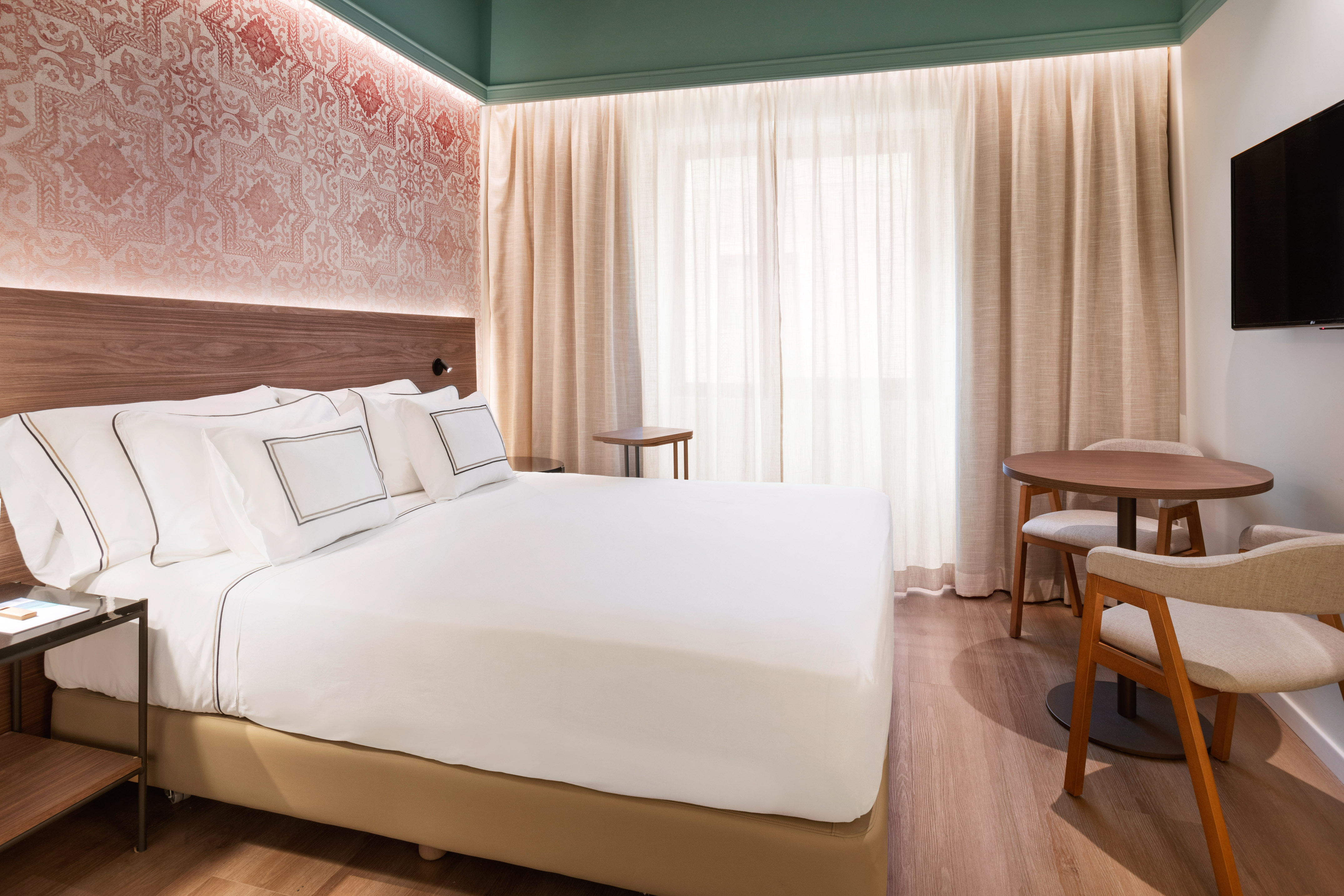 Modern hotel room with queen bed, decorative wallpaper, and cozy dining area.