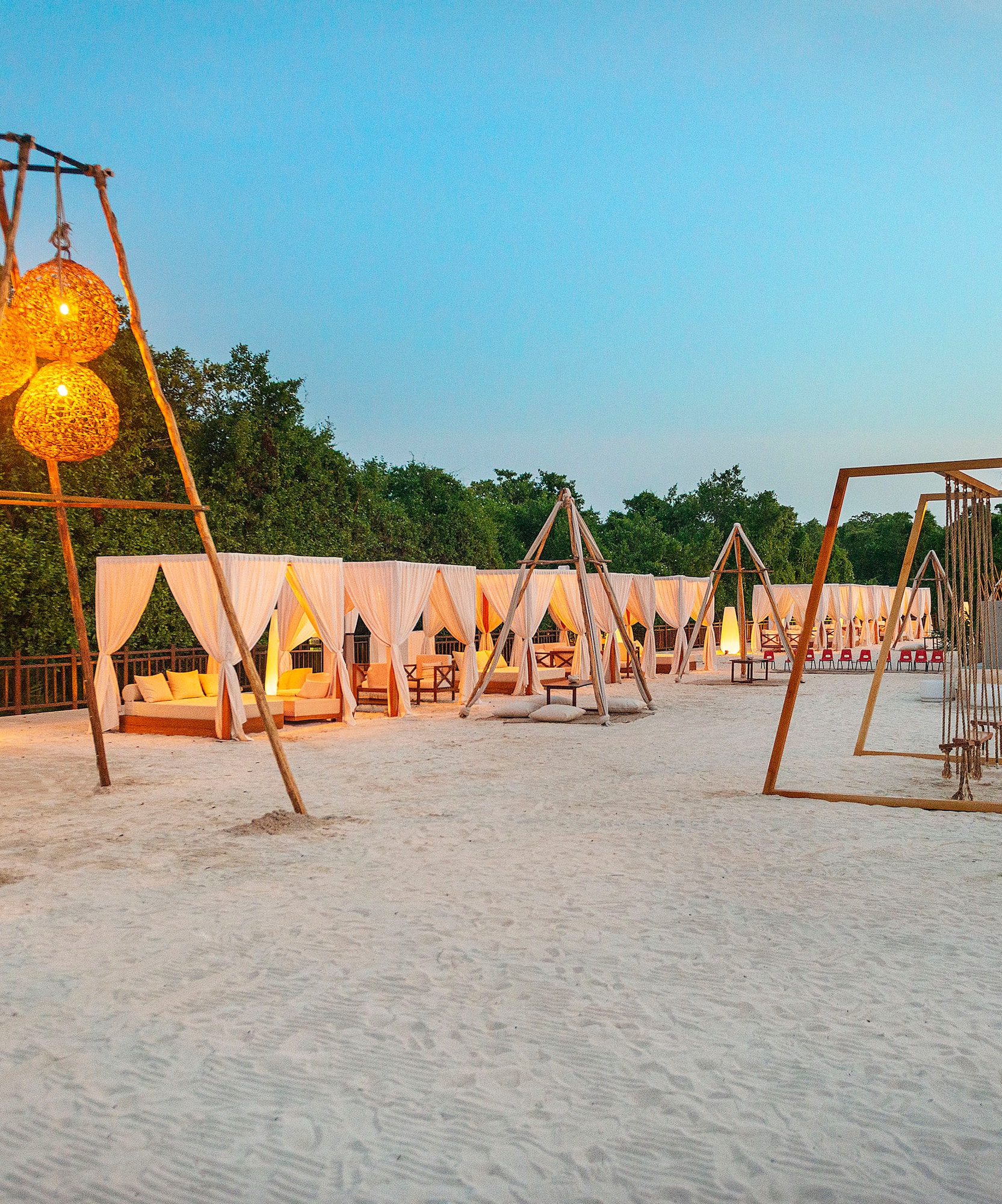 Cabañas y faroles iluminados sobre arena blanca al atardecer en resort.