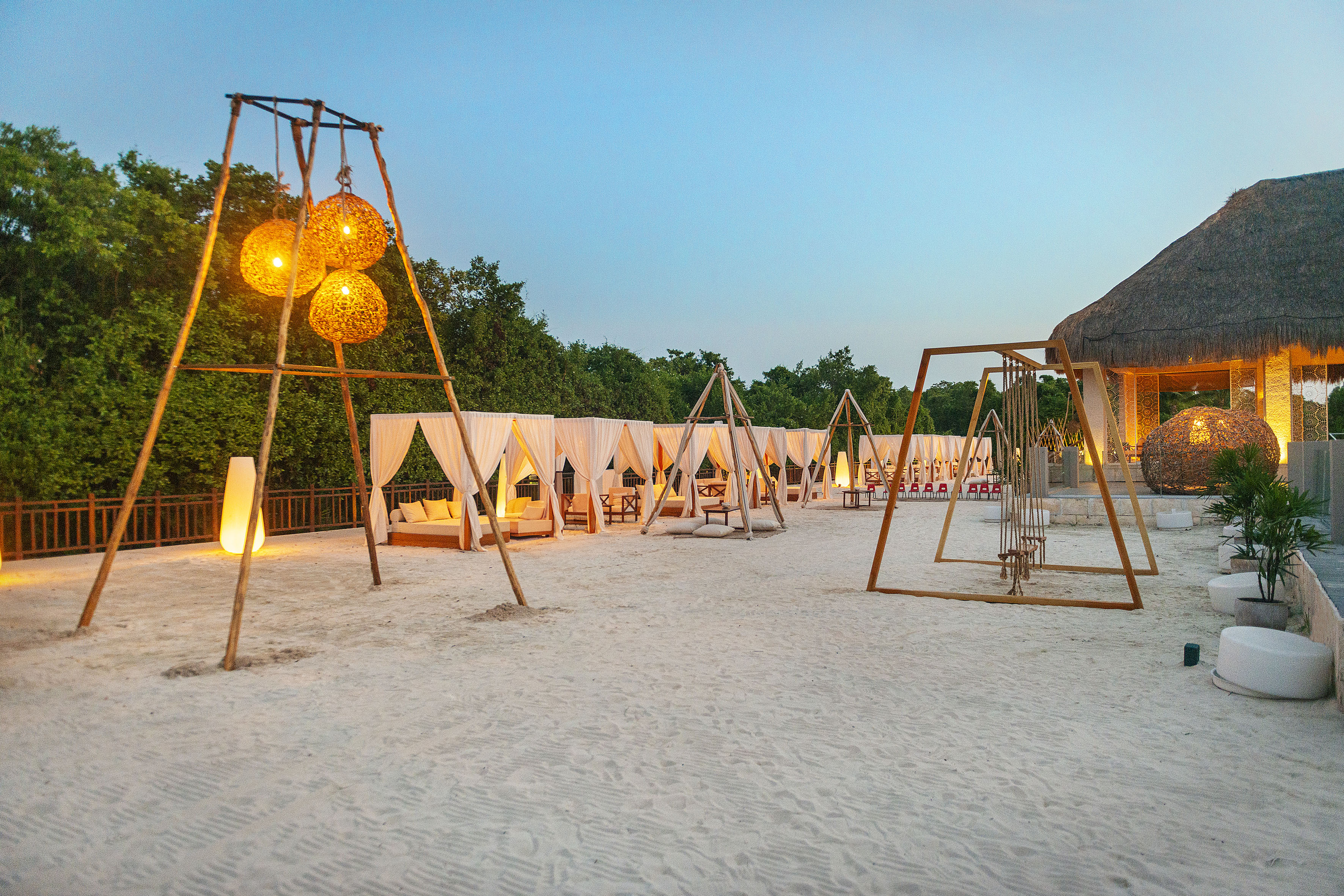 Cabañas y faroles iluminados sobre arena blanca al atardecer en resort.