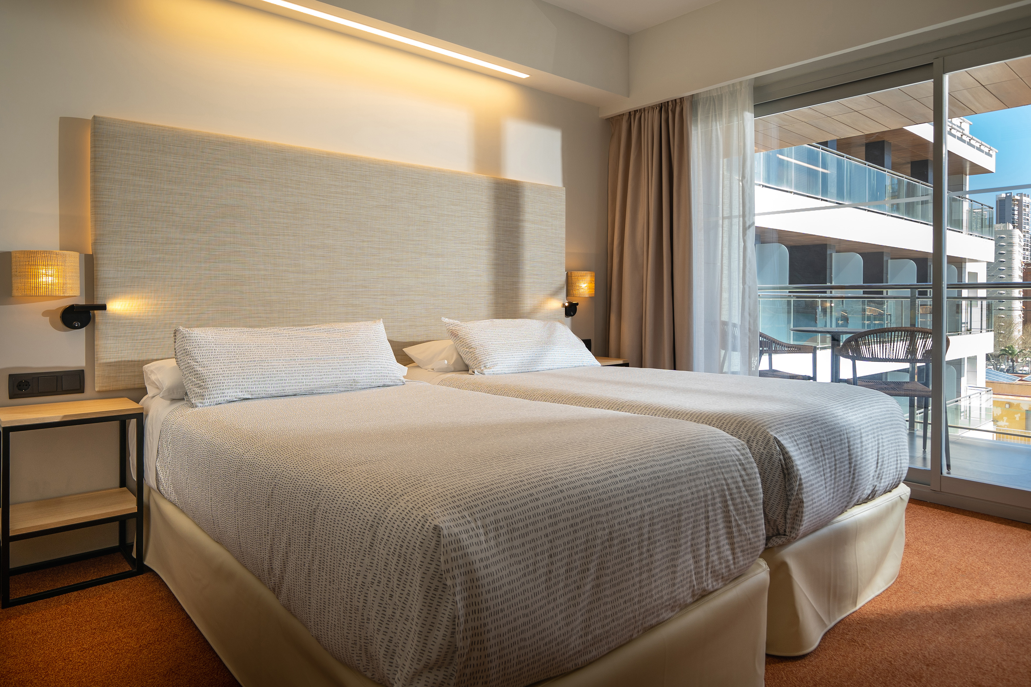Modern hotel room with twin beds, balcony, and city view.