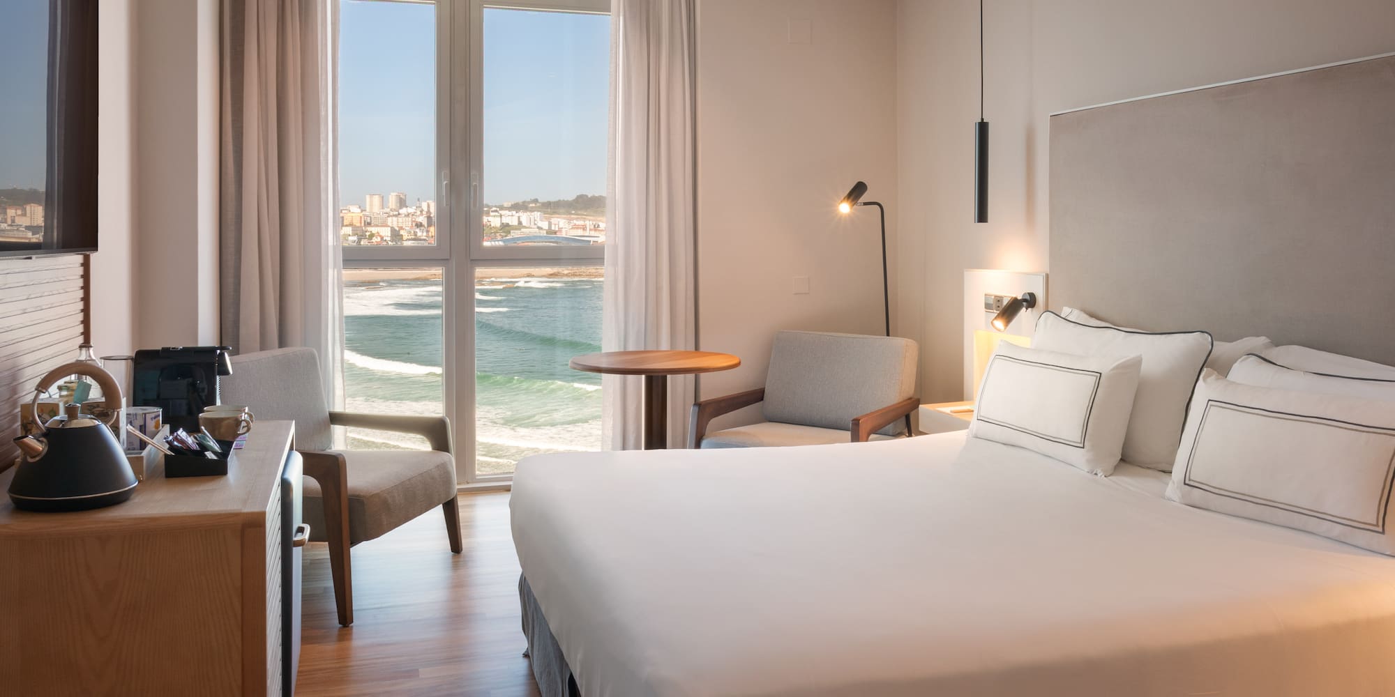 Habitación de hotel moderna con cama, vistas al mar y ciudad.