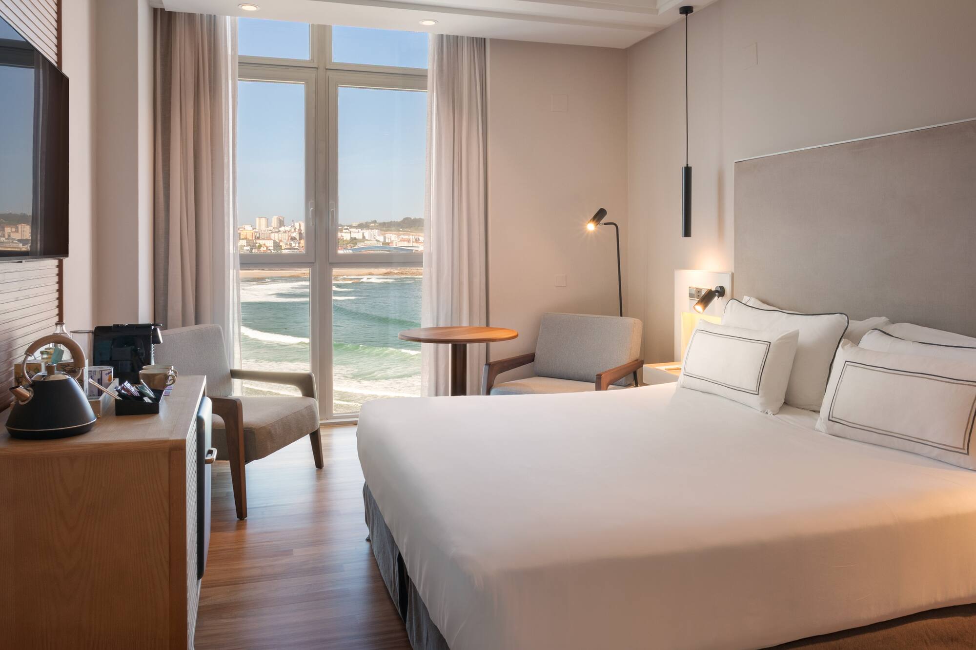 Habitación de hotel moderna con cama, vistas al mar y ciudad.