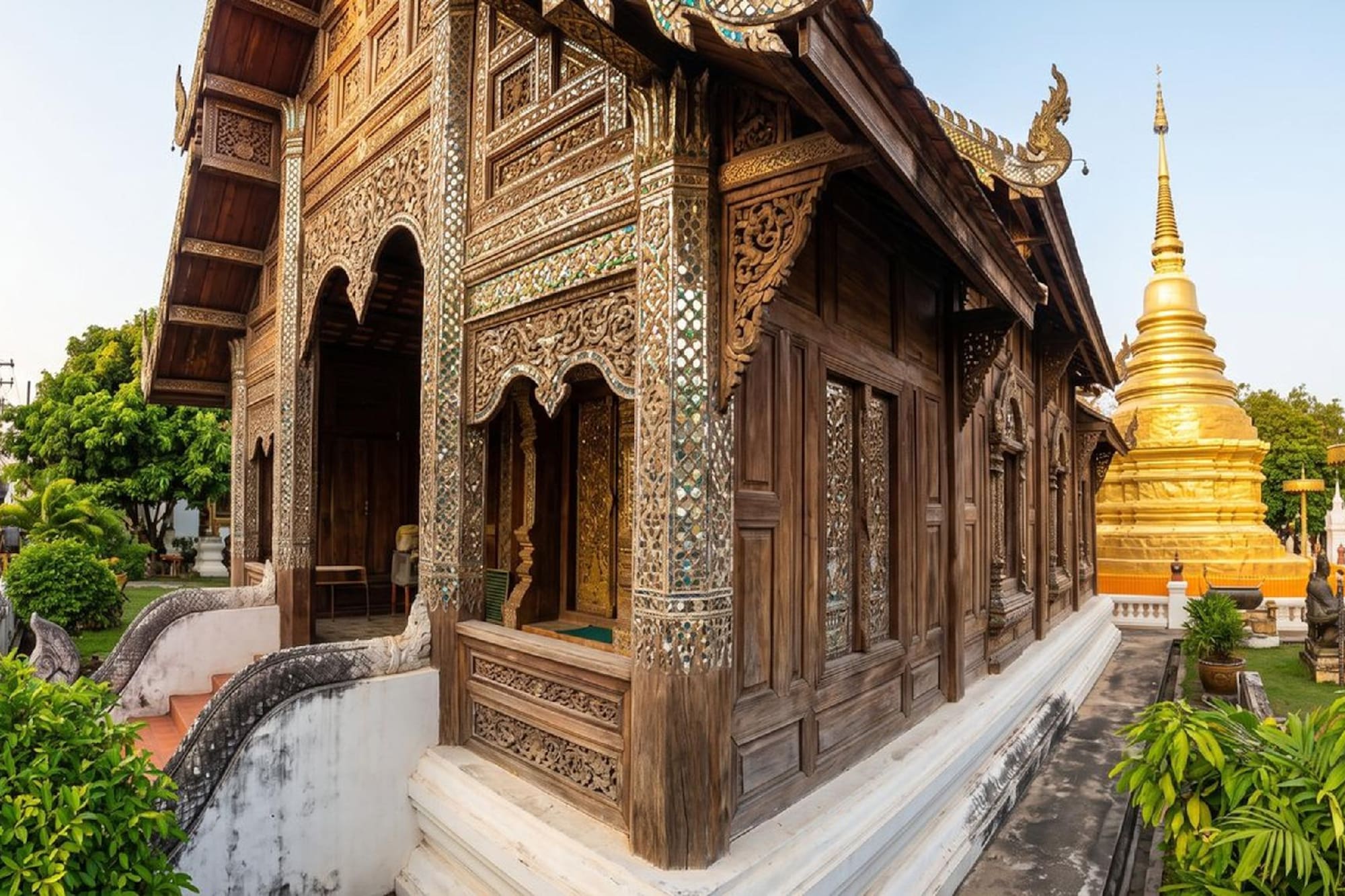 Ornate wooden Thai temple with intricate carvings and golden stupa.