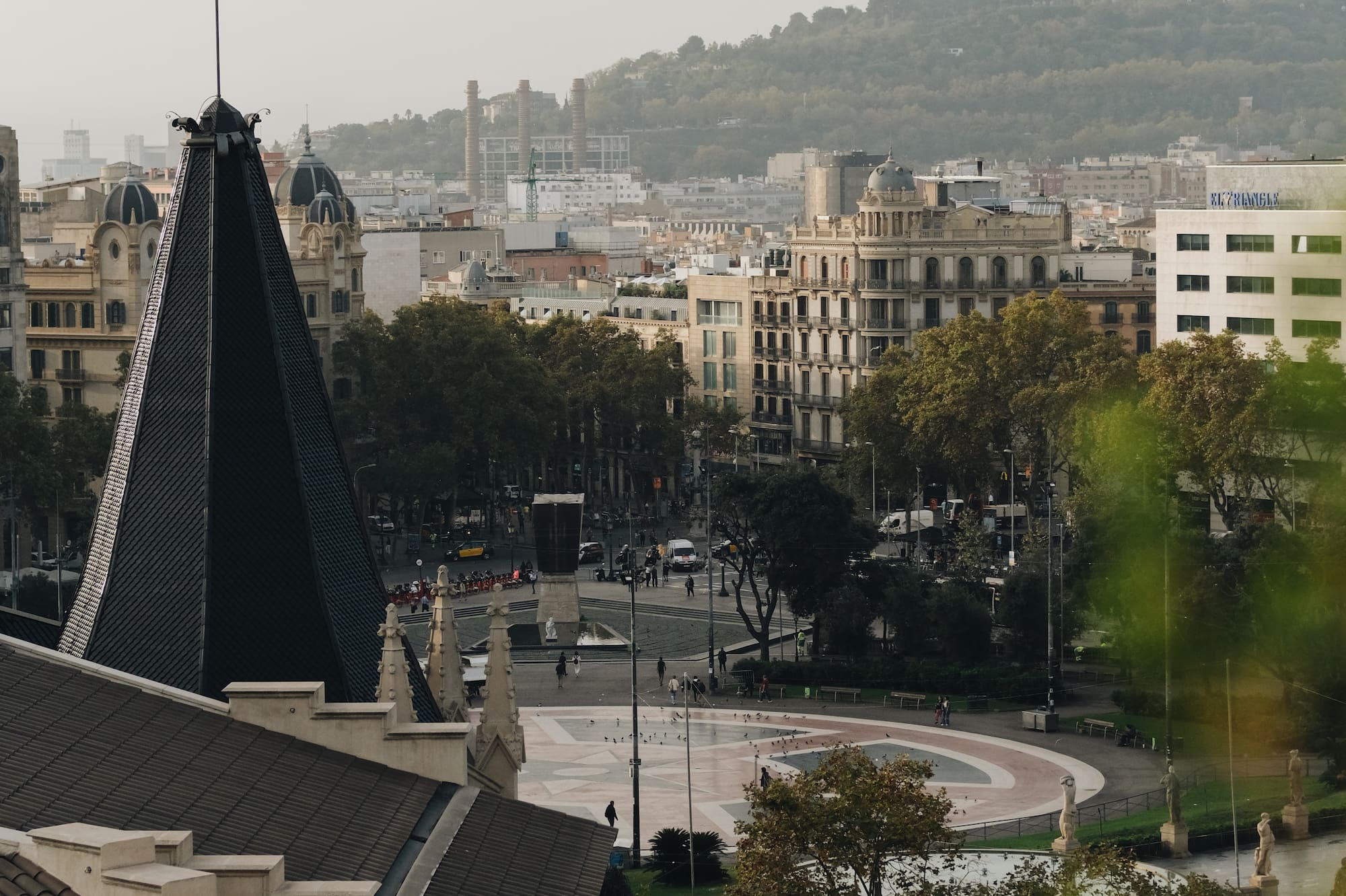 Panorama de Plaça Catalunya, Barcelona: tejado con veleta, edificios, montaña.