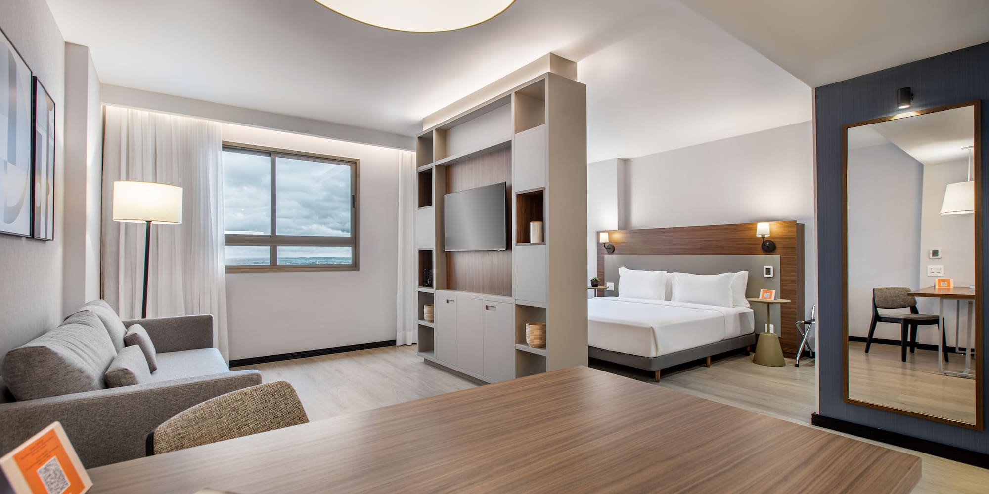 Modern hotel studio suite with bed, sofa, TV, and desk.